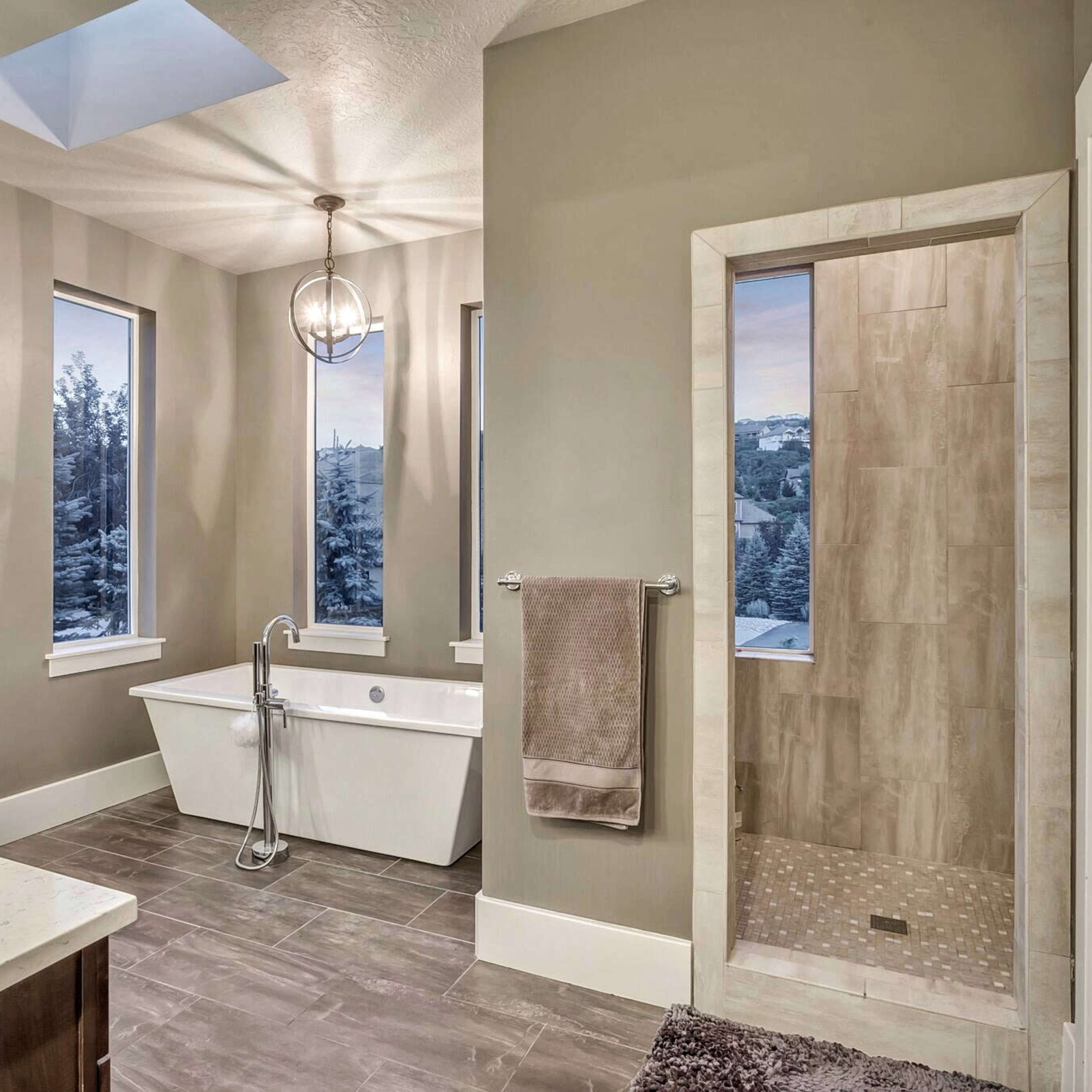 A modern bathroom featuring a freestanding bathtub, a glass-enclosed shower, and large windows allowing natural light.