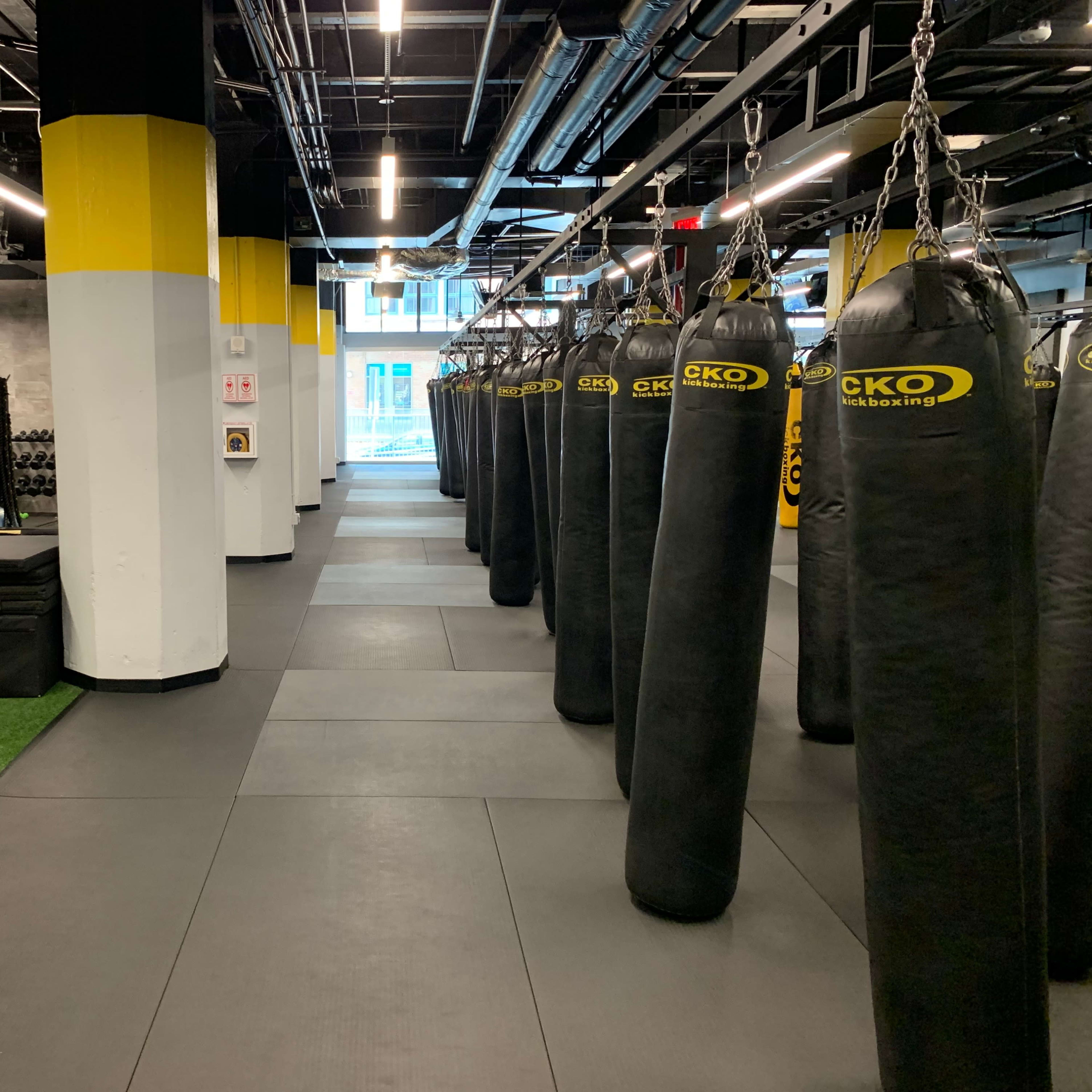 A fitness facility with rows of heavy punching bags, a turf area with equipment, and exercise mats.