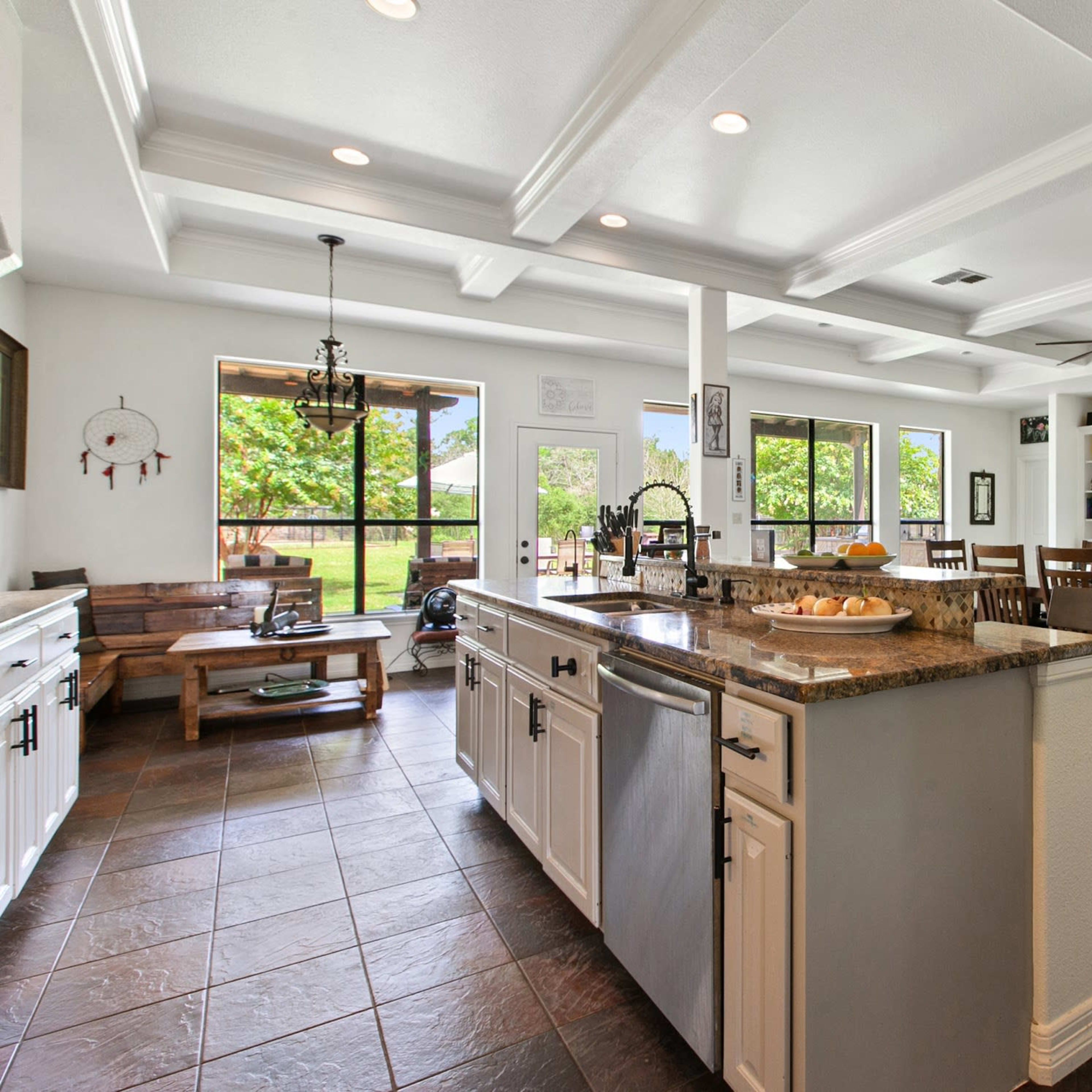 A spacious kitchen and dining area featuring white cabinetry, a central island with granite countertops, and large windows overlooking a green landscape.