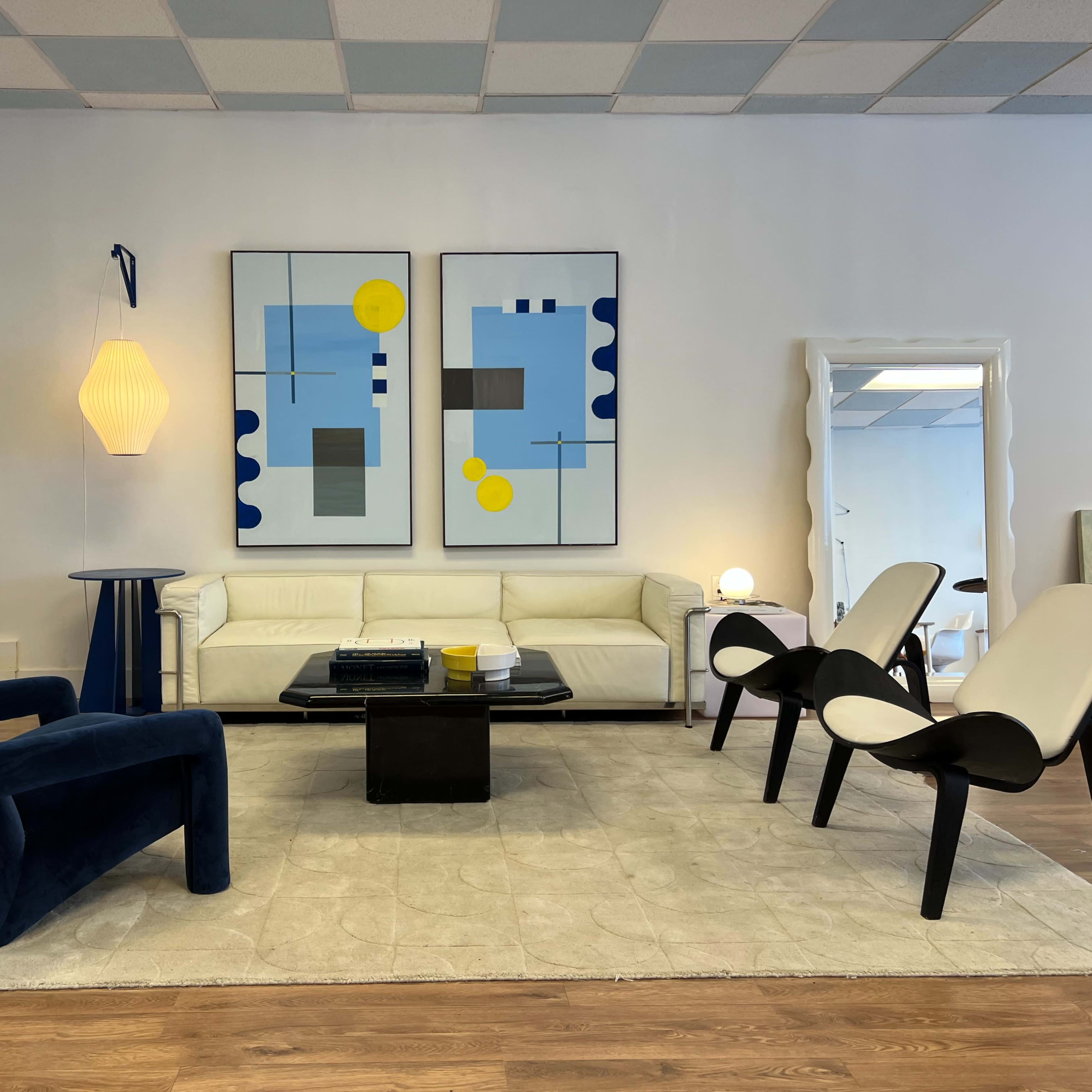 A modern living room with a white sofa, black coffee table, and two stylized chairs arranged on a light-colored rug, featuring abstract artwork on the walls.