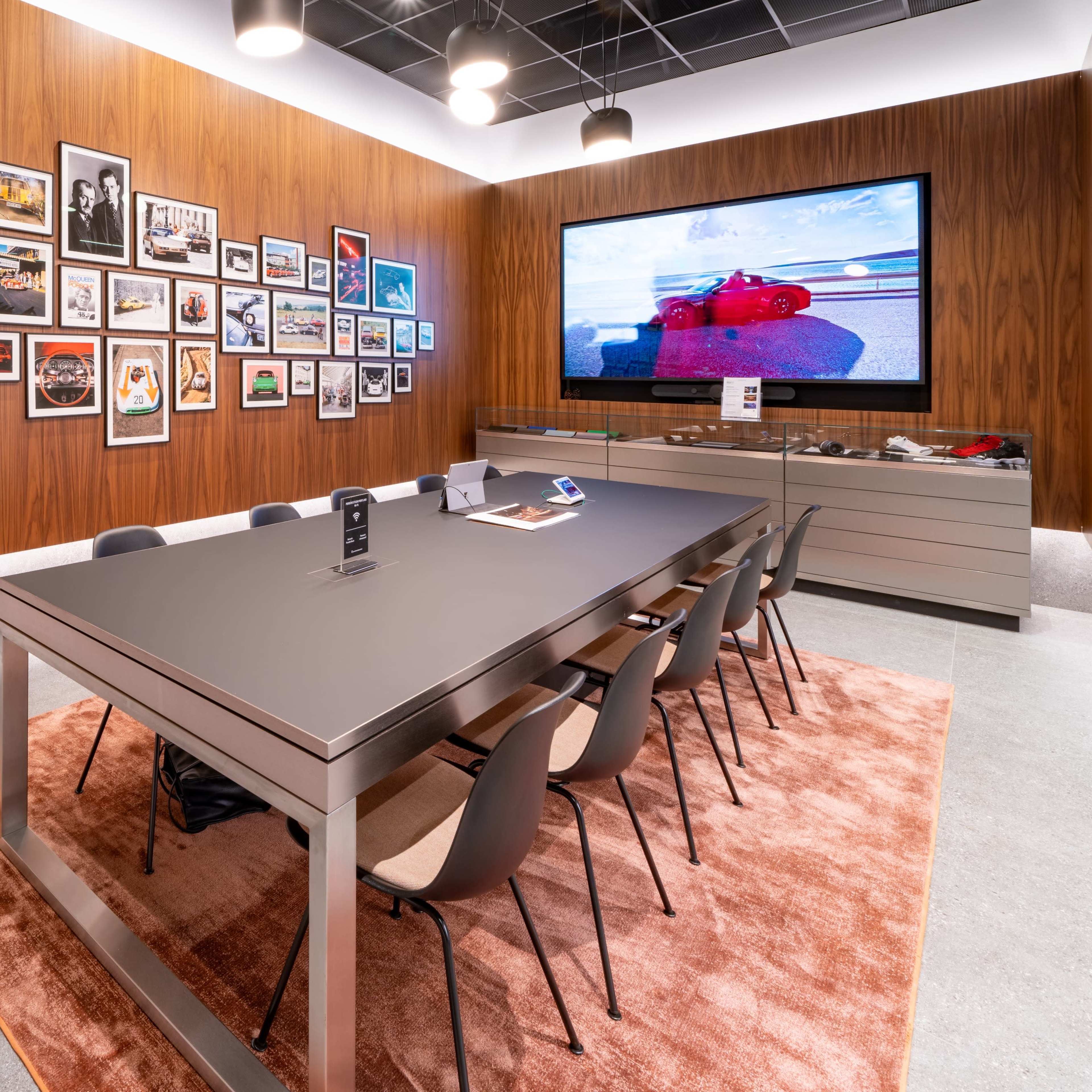 A modern conference room featuring a long table with chairs, a large television screen displaying images, and a wall adorned with framed photographs.
