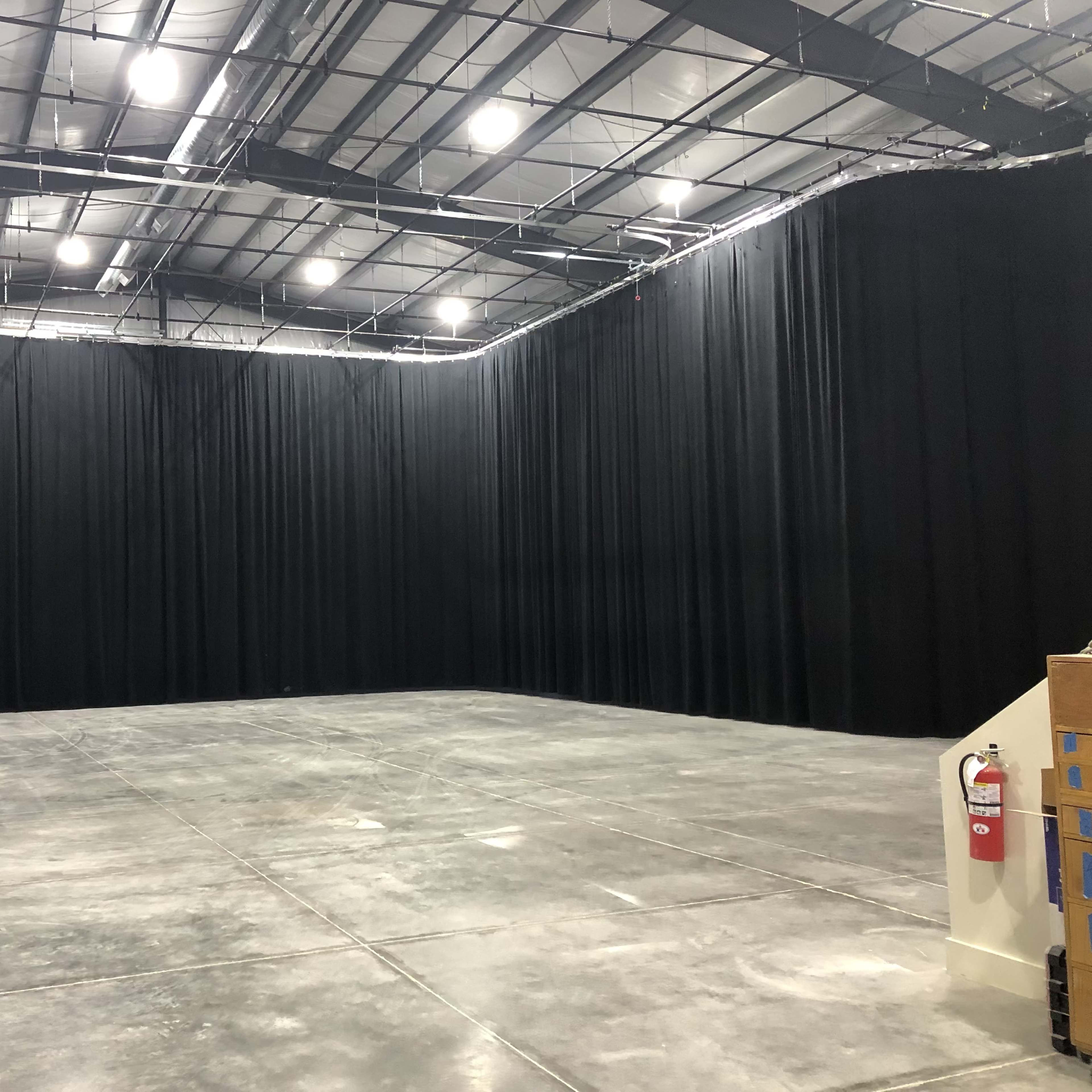 A large studio space with black curtain walls, a concrete floor, and overhead lighting.
