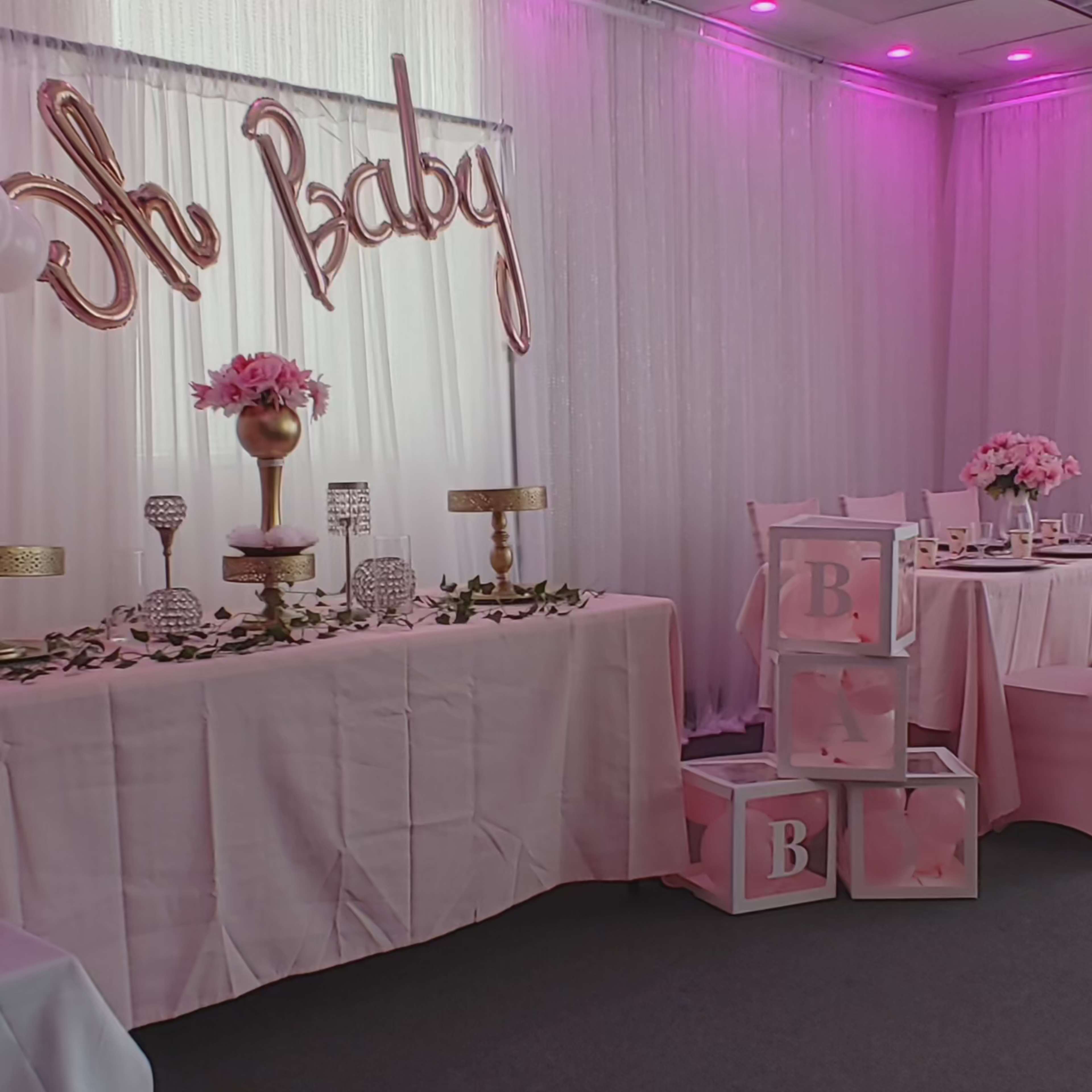 A decorated event space with a "Oh Baby" sign, floral centerpieces, and stacked boxes featuring the letter "B."