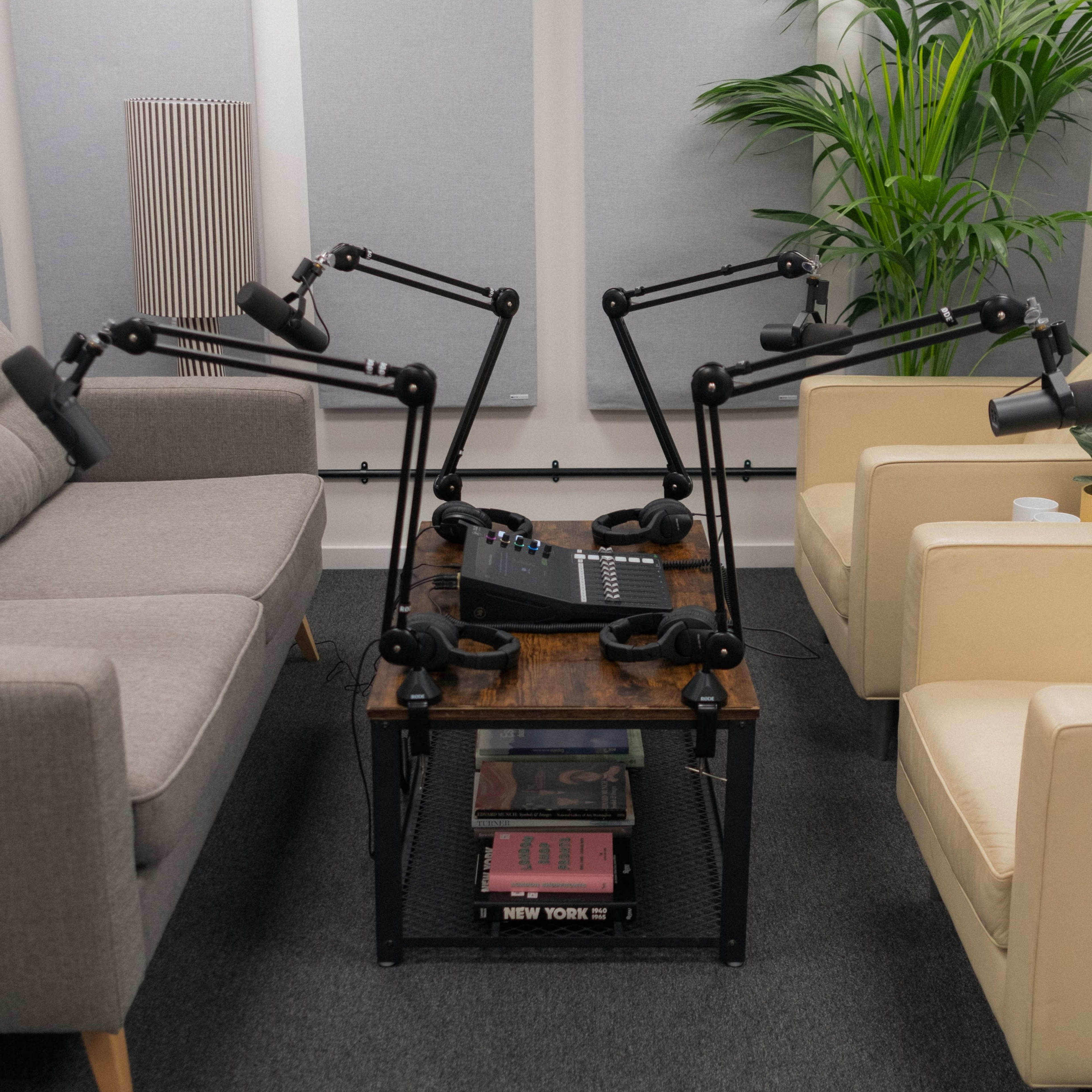 A podcasting setup features a wooden table with sound equipment surrounded by two armchairs and soundproofing panels.