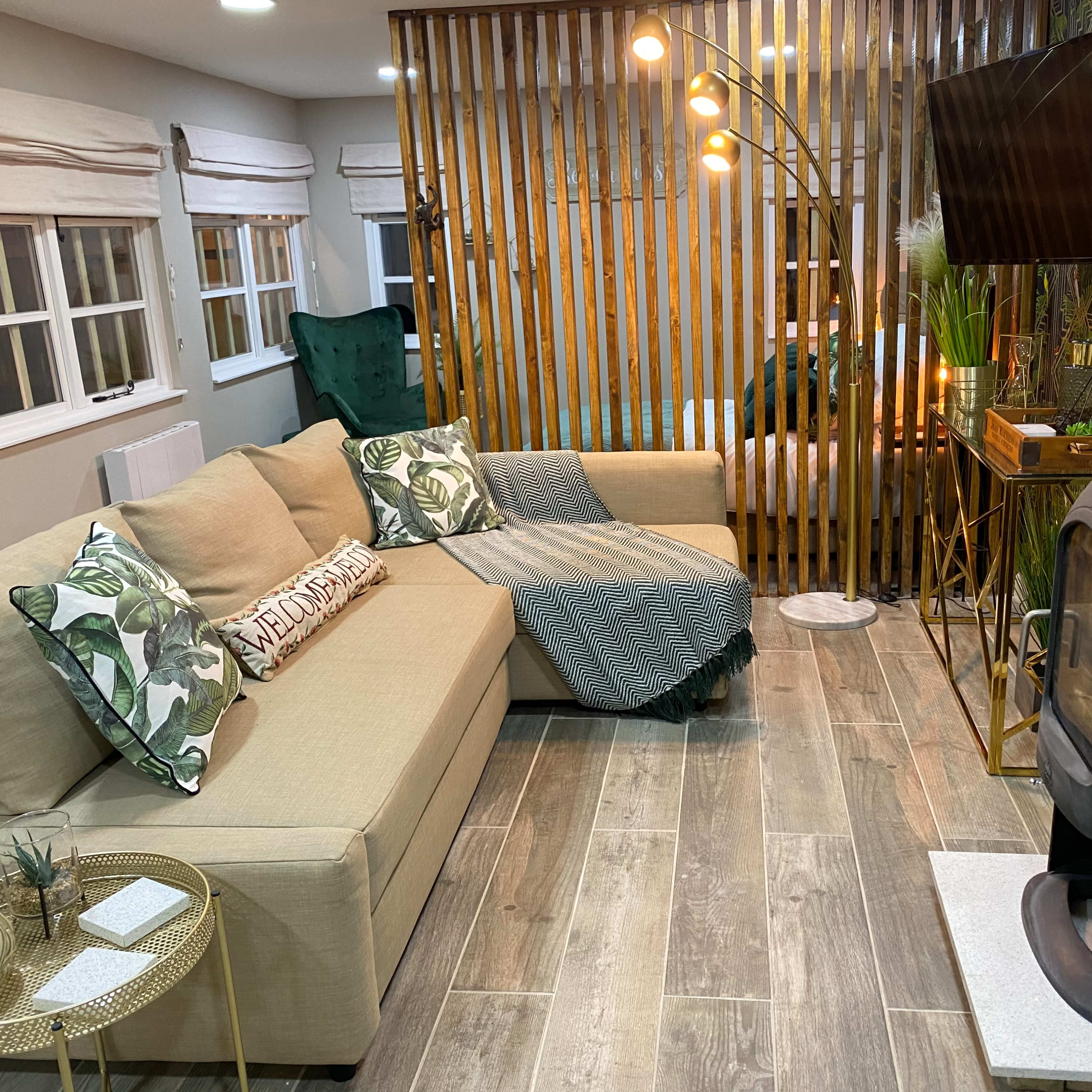 A cozy living area with a sectional sofa, a standing lamp, a television mounted on a wooden divider, and a modern wood stove.