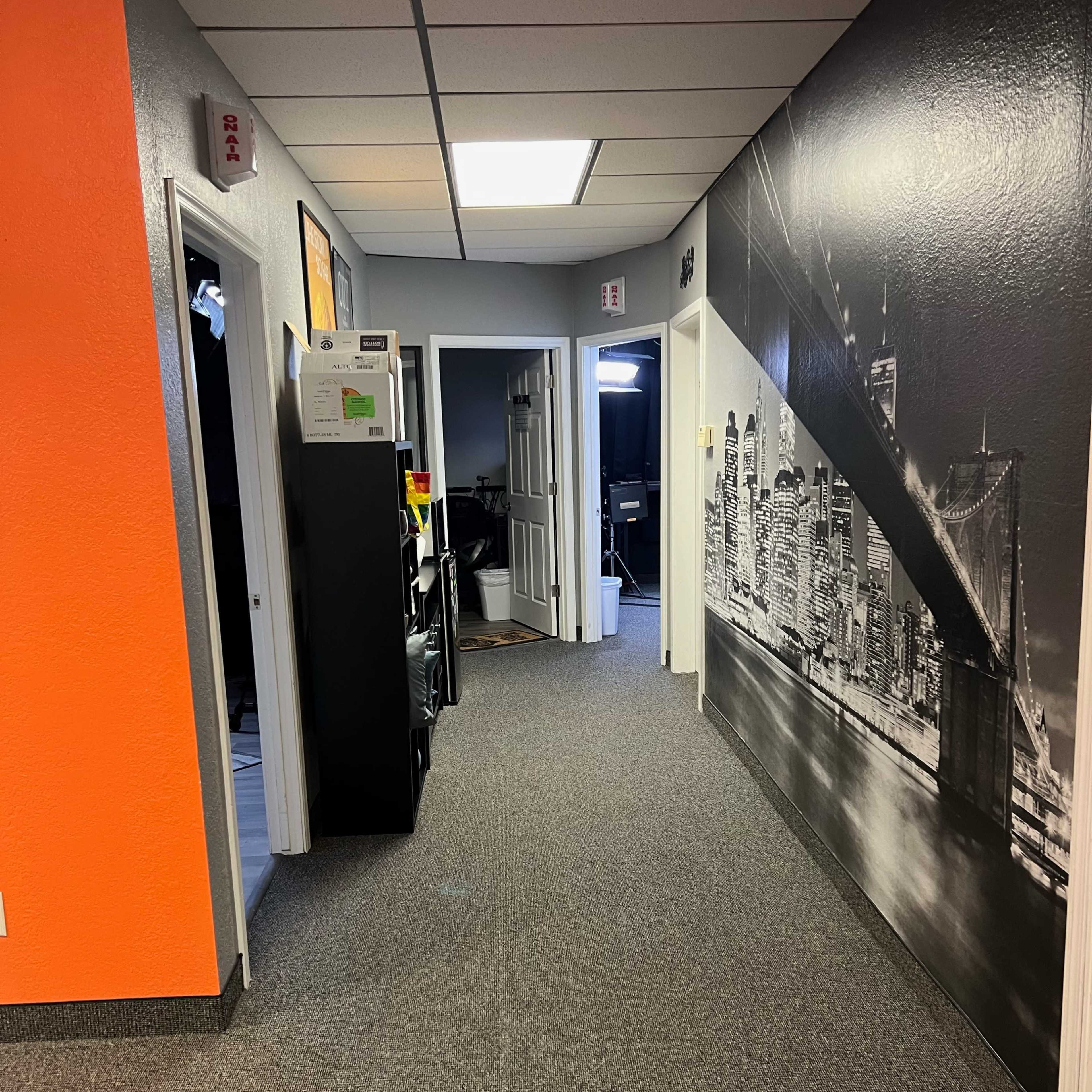 A hallway with orange and gray walls, featuring several doors, a black storage cabinet, and a large black-and-white mural of a city skyline.