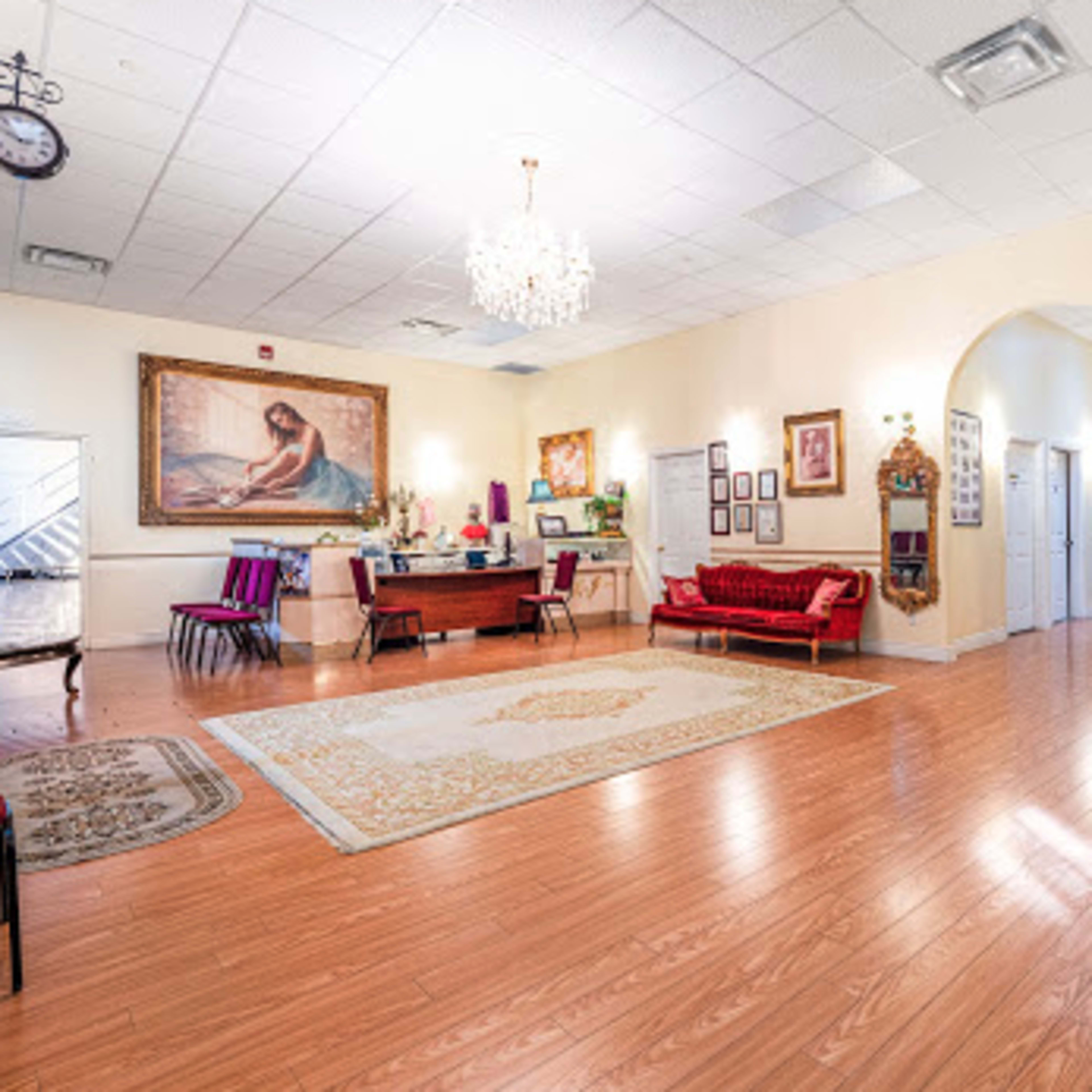 A spacious reception area with hardwood floors, a large ornate painting on the wall, a chandelier, and a mix of seating arrangements.