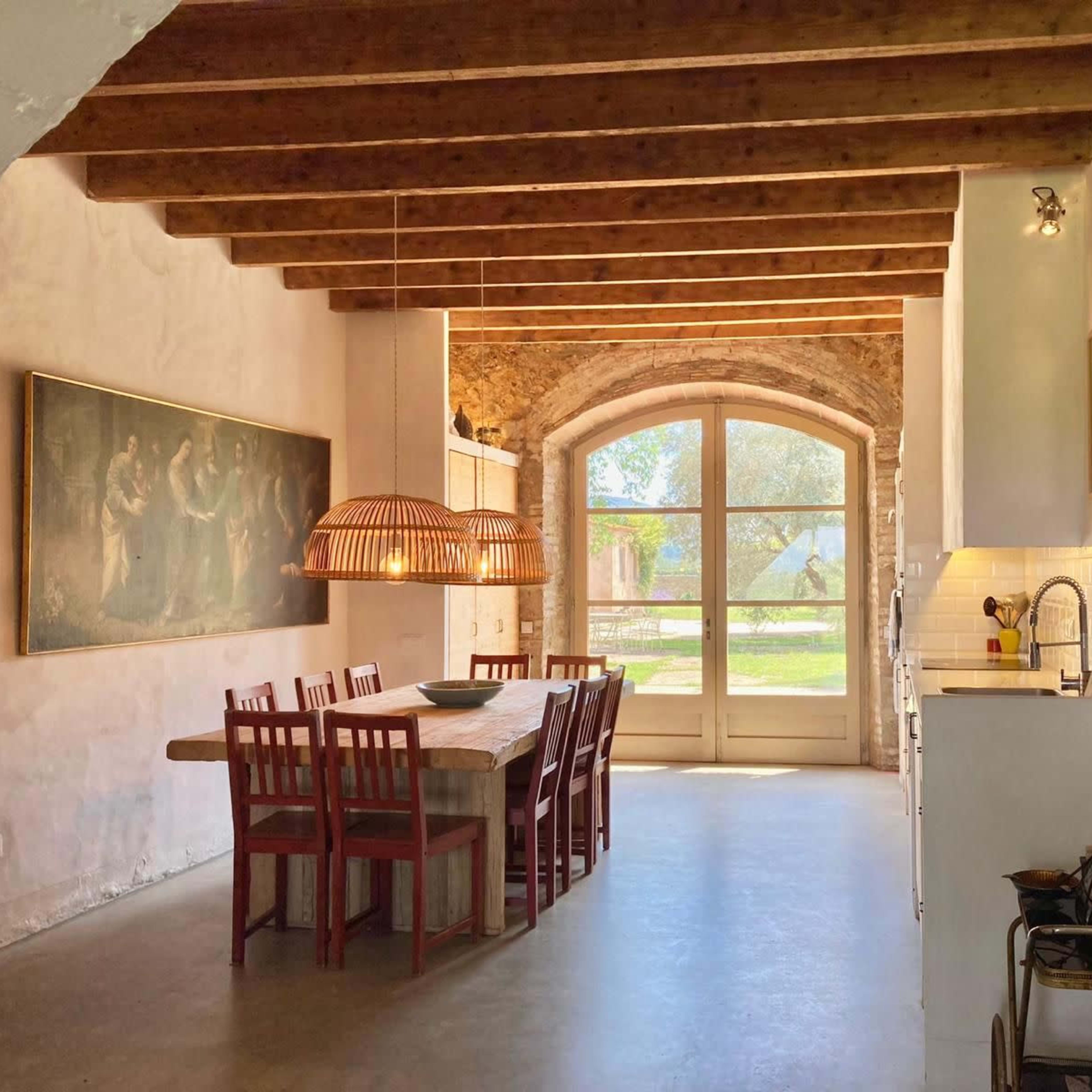 A modern kitchen and dining area with a wooden table, chairs, and large windows that provide a view of the outdoors.