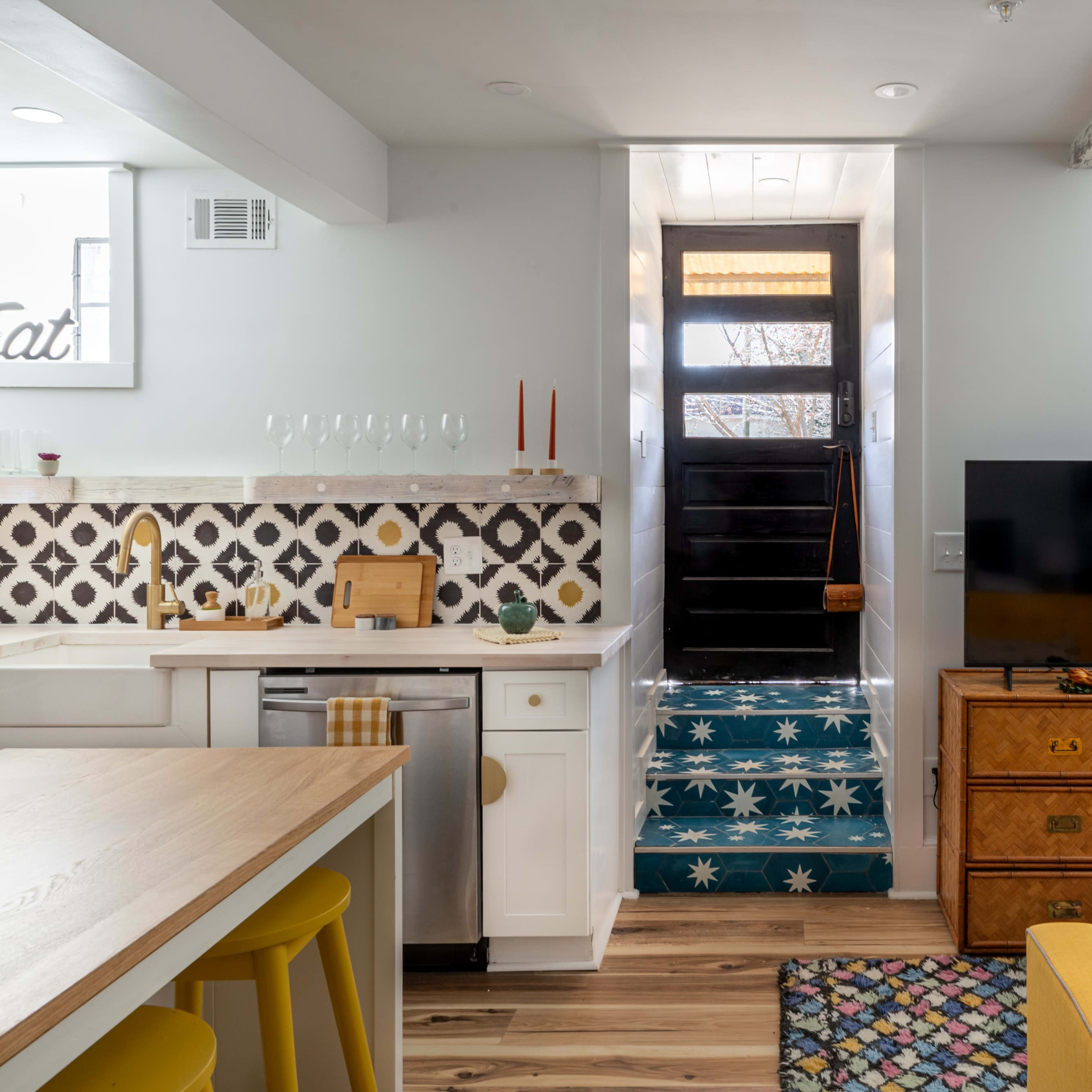 A modern living space with a dining area, a staircase leading to a door, and a television beside a chest of drawers.