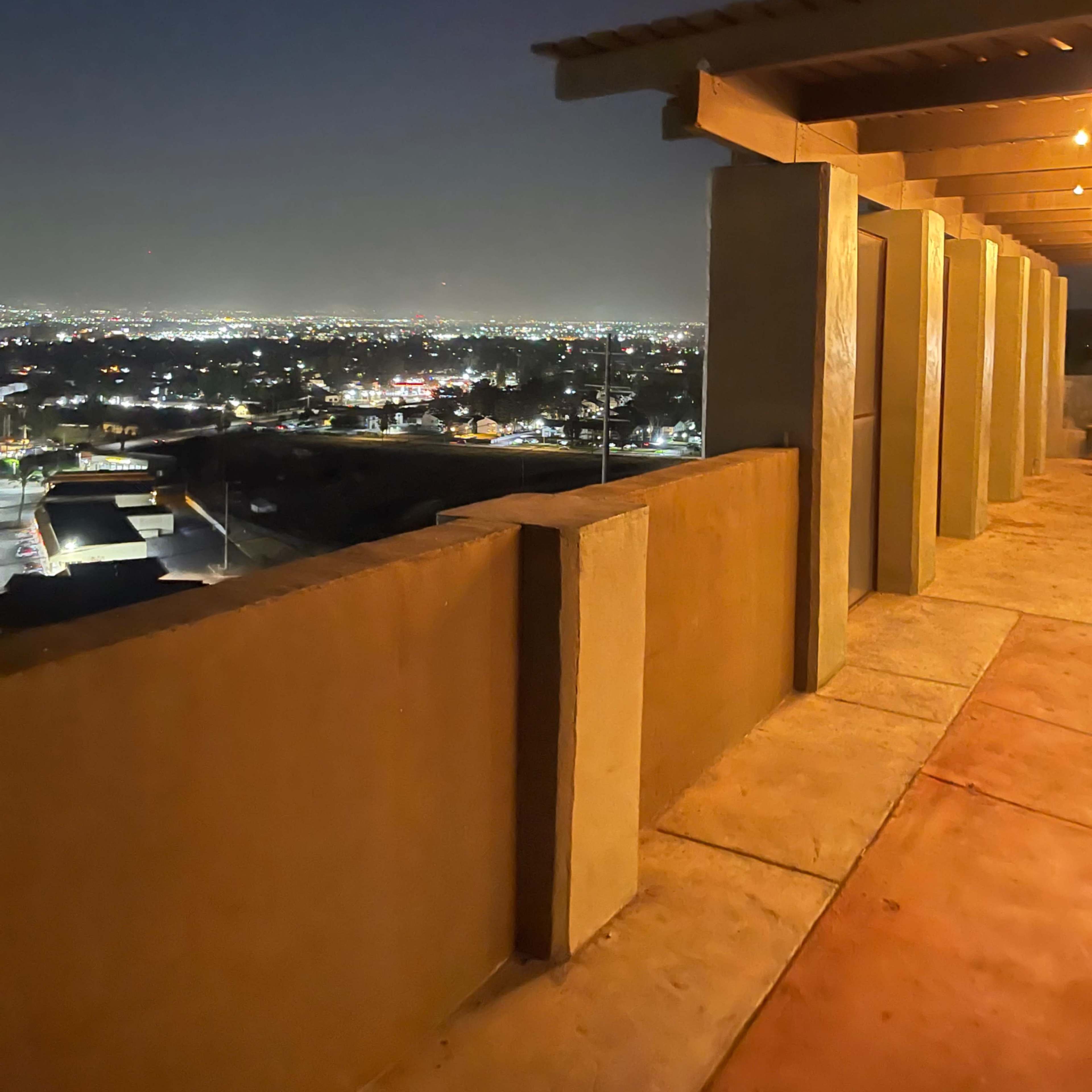 A dimly lit balcony overlooks a city skyline at night, with lights twinkling in the distance.