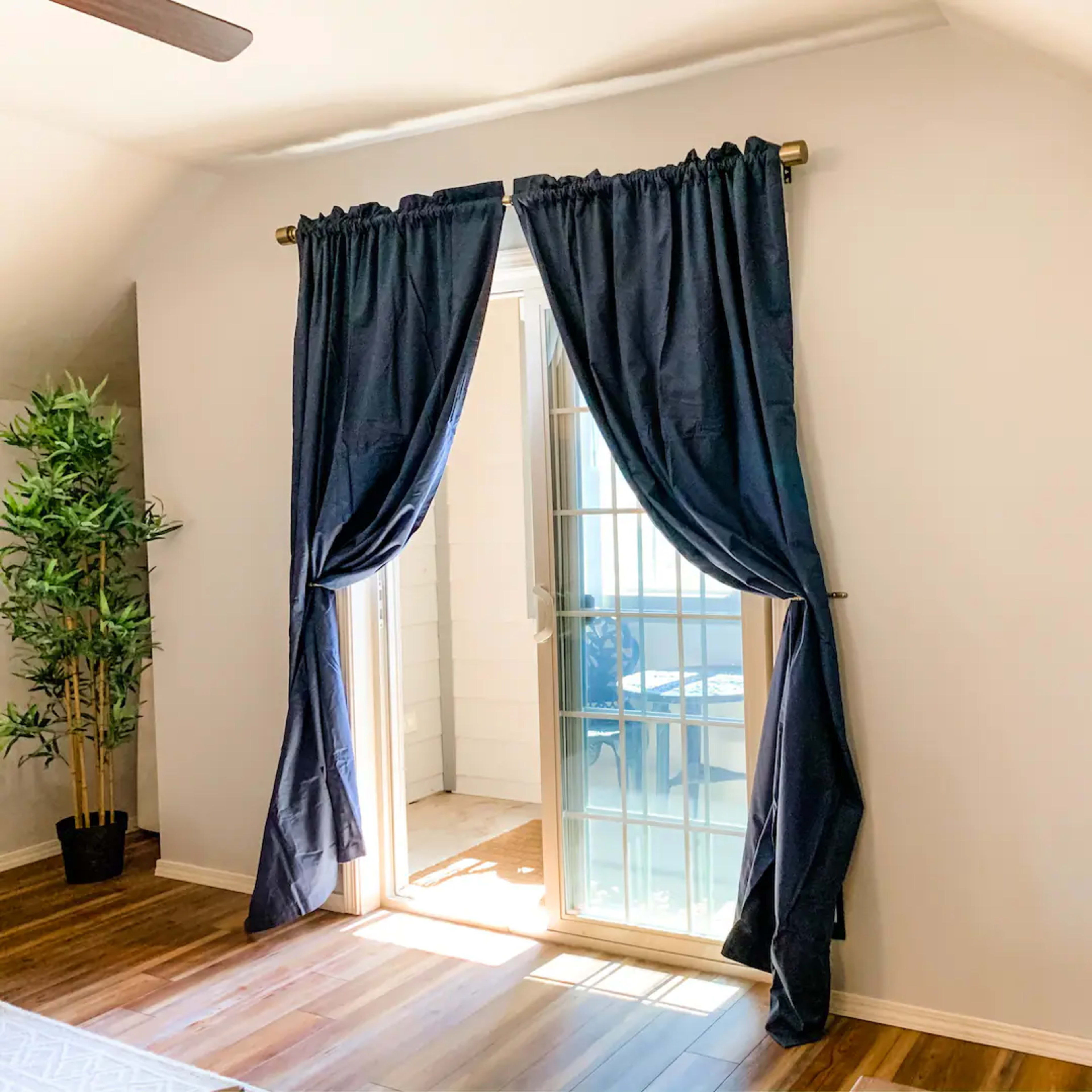 A sunlit room features a sliding glass door with navy curtains and a bookshelf filled with books against a light-colored wall.