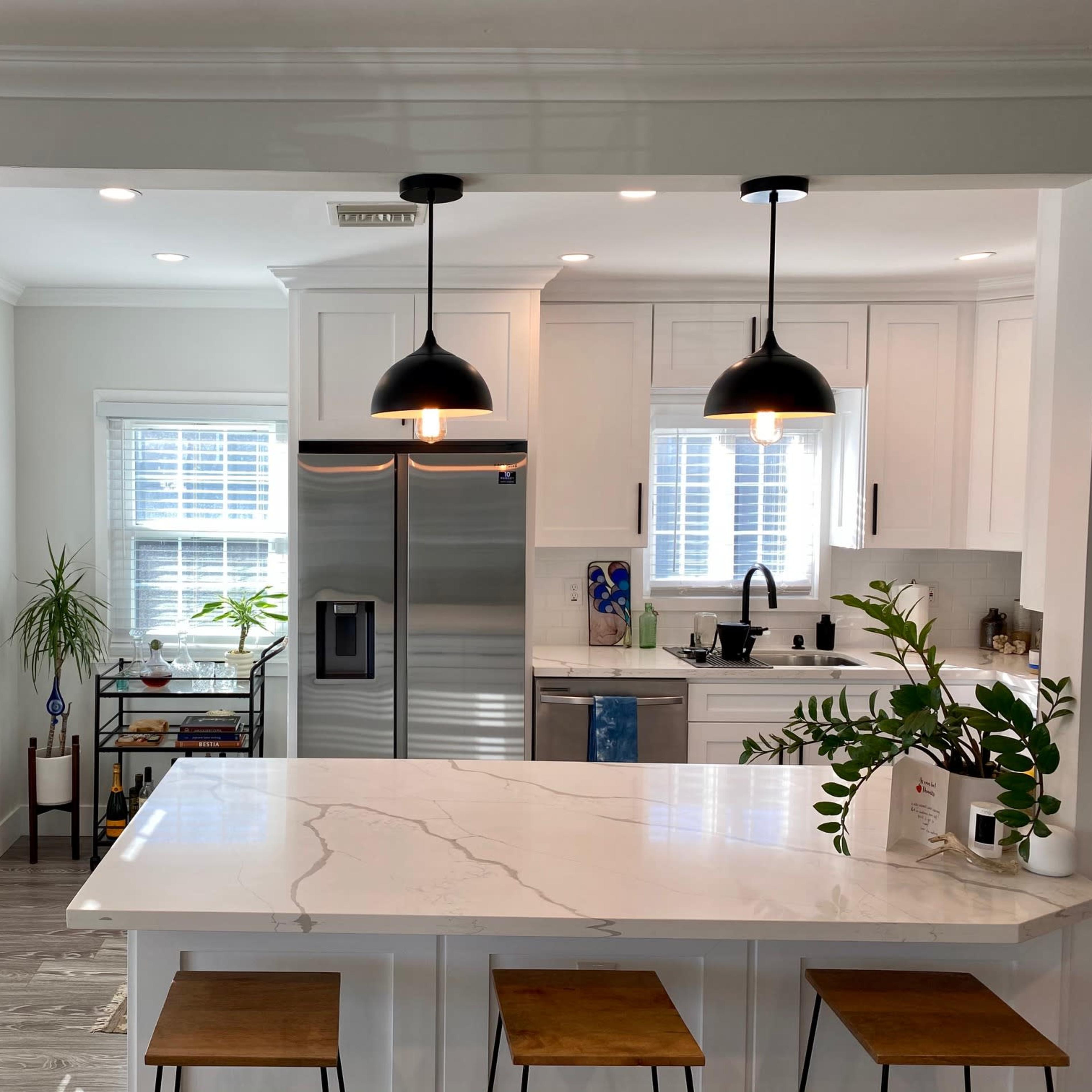 A bright kitchen features white cabinetry, stainless steel appliances, and a marble island with three wooden stools.