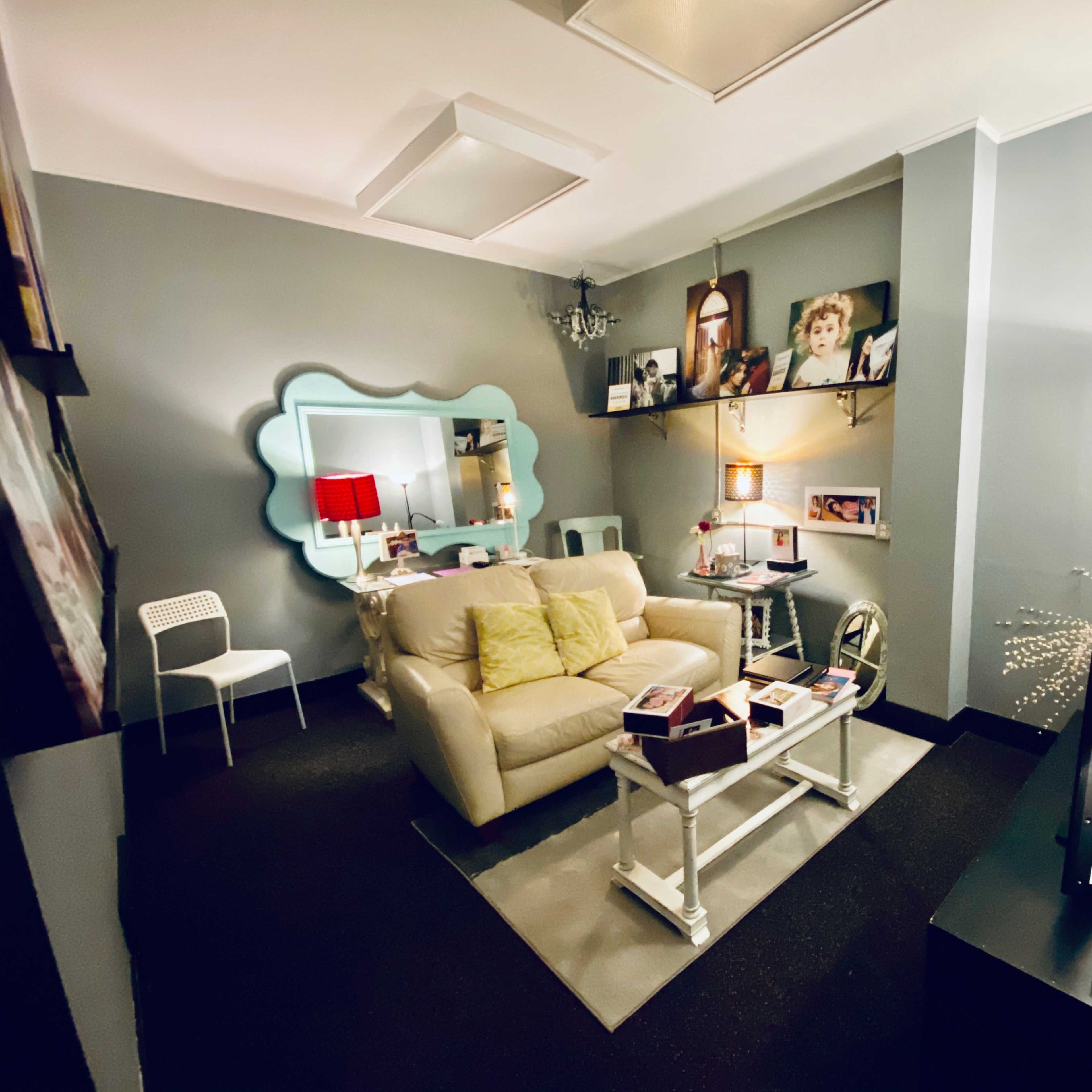 A small, well-lit lounge area featuring a beige sofa, a coffee table with decorative items, and framed photos on the wall.