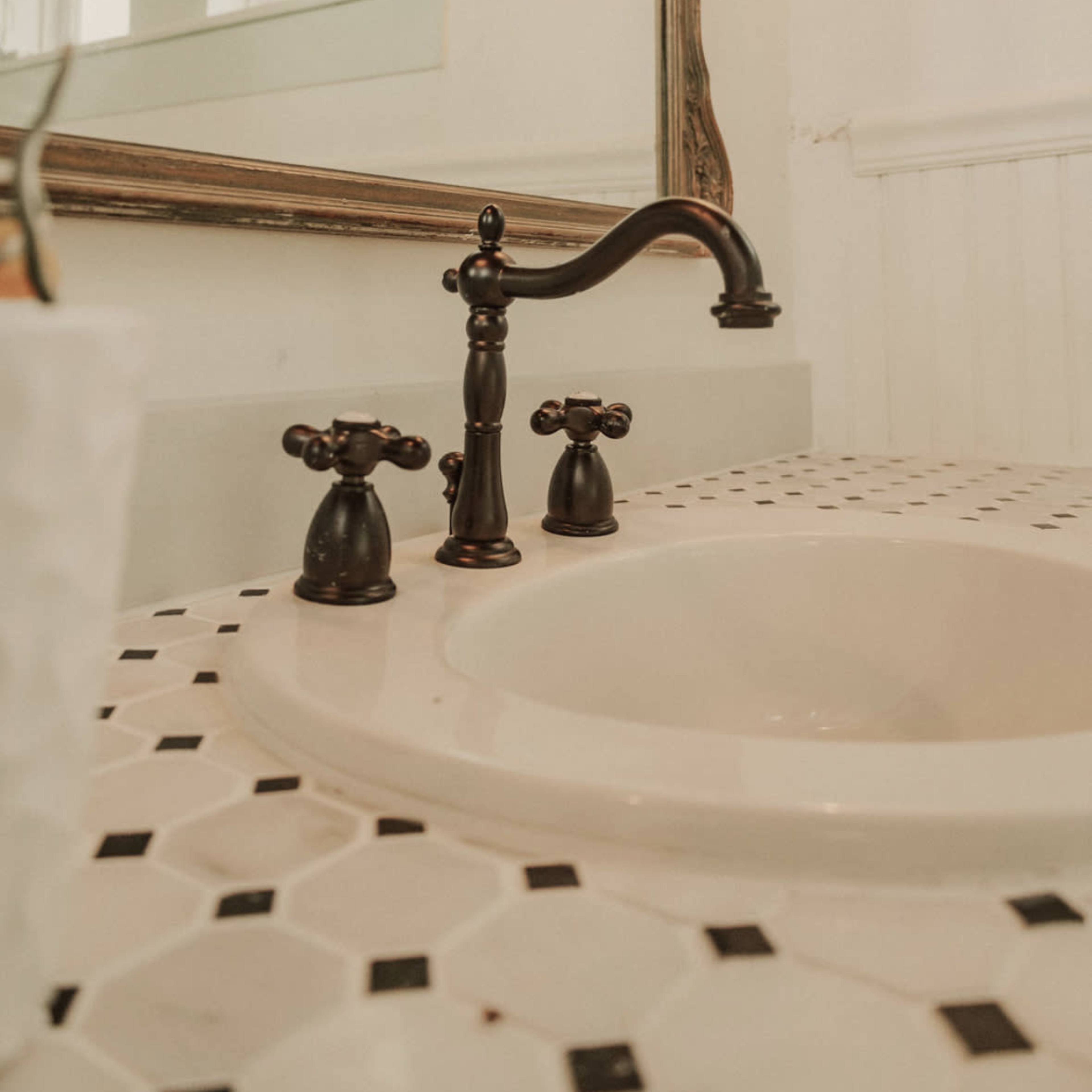 A close-up of a bathroom sink with a black faucet and black and white hexagonal tile surrounding it.