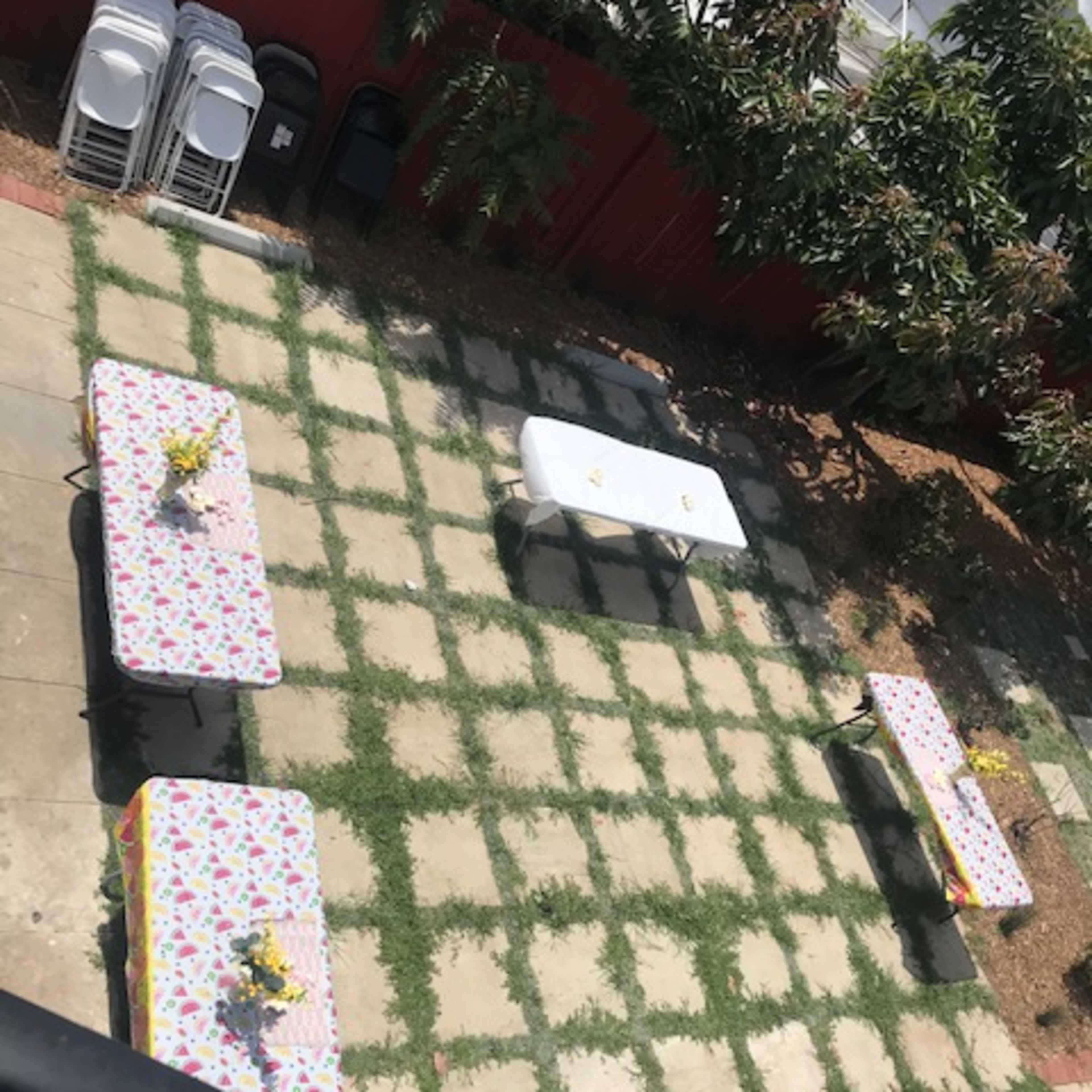 A backyard with several tables covered in floral tablecloths arranged on a grassy stone patio.