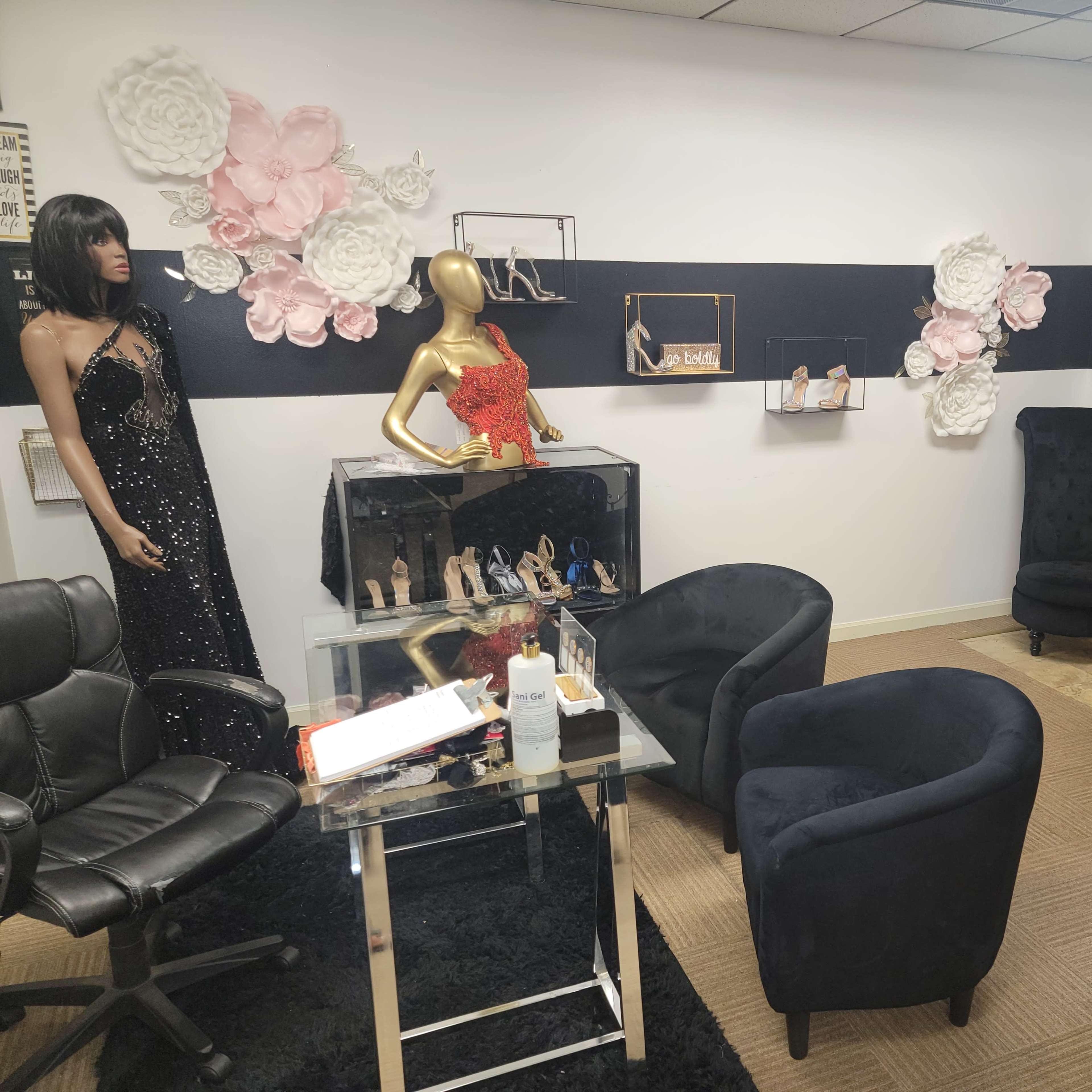 A boutique interior featuring a black carpet, a seating area with two chairs, a mannequin dressed in a sequined gown, and decorative floral accents on the wall.