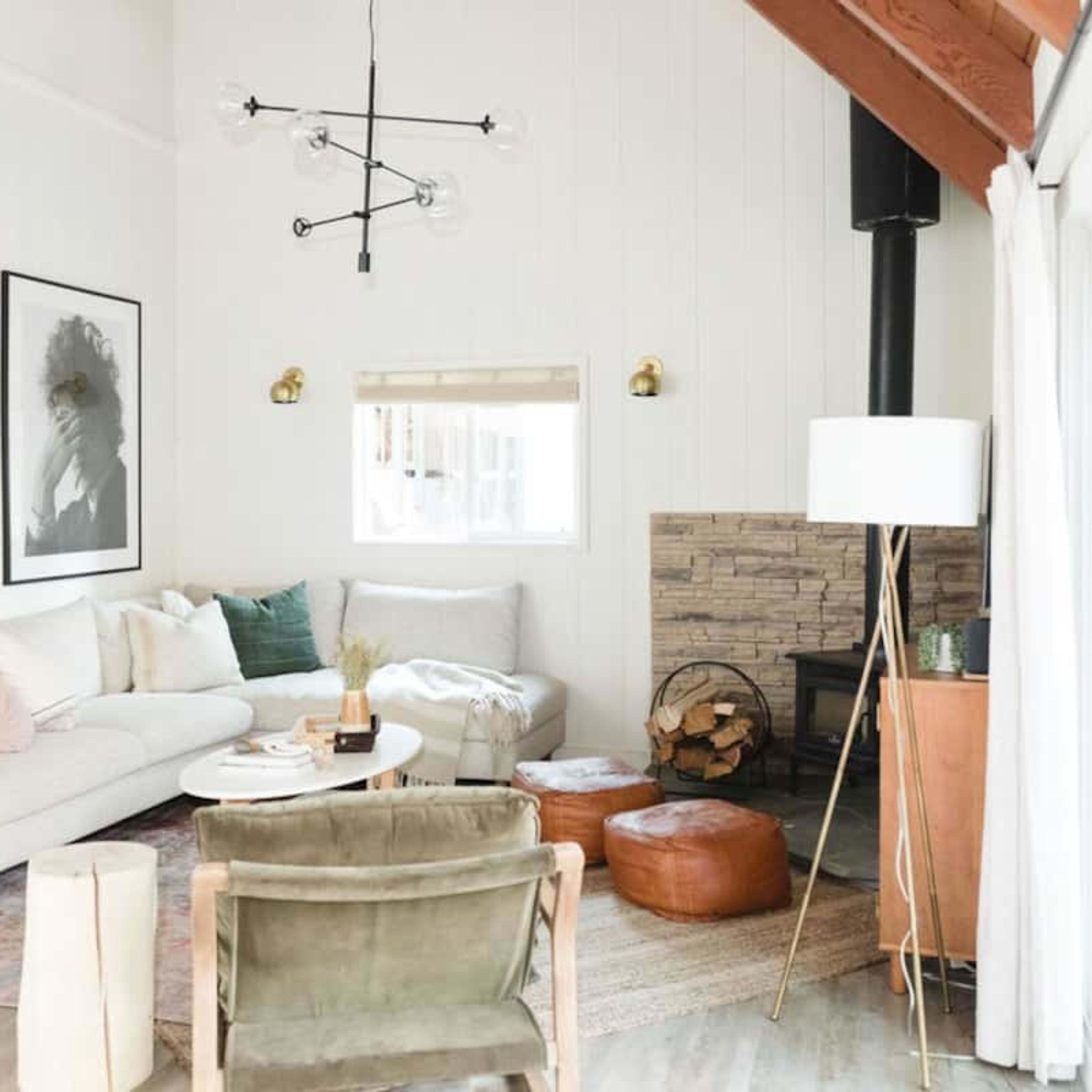 A light-filled living room features a white sofa, round coffee table, and a fireplace surrounded by wood, complemented by modern artwork on the walls.