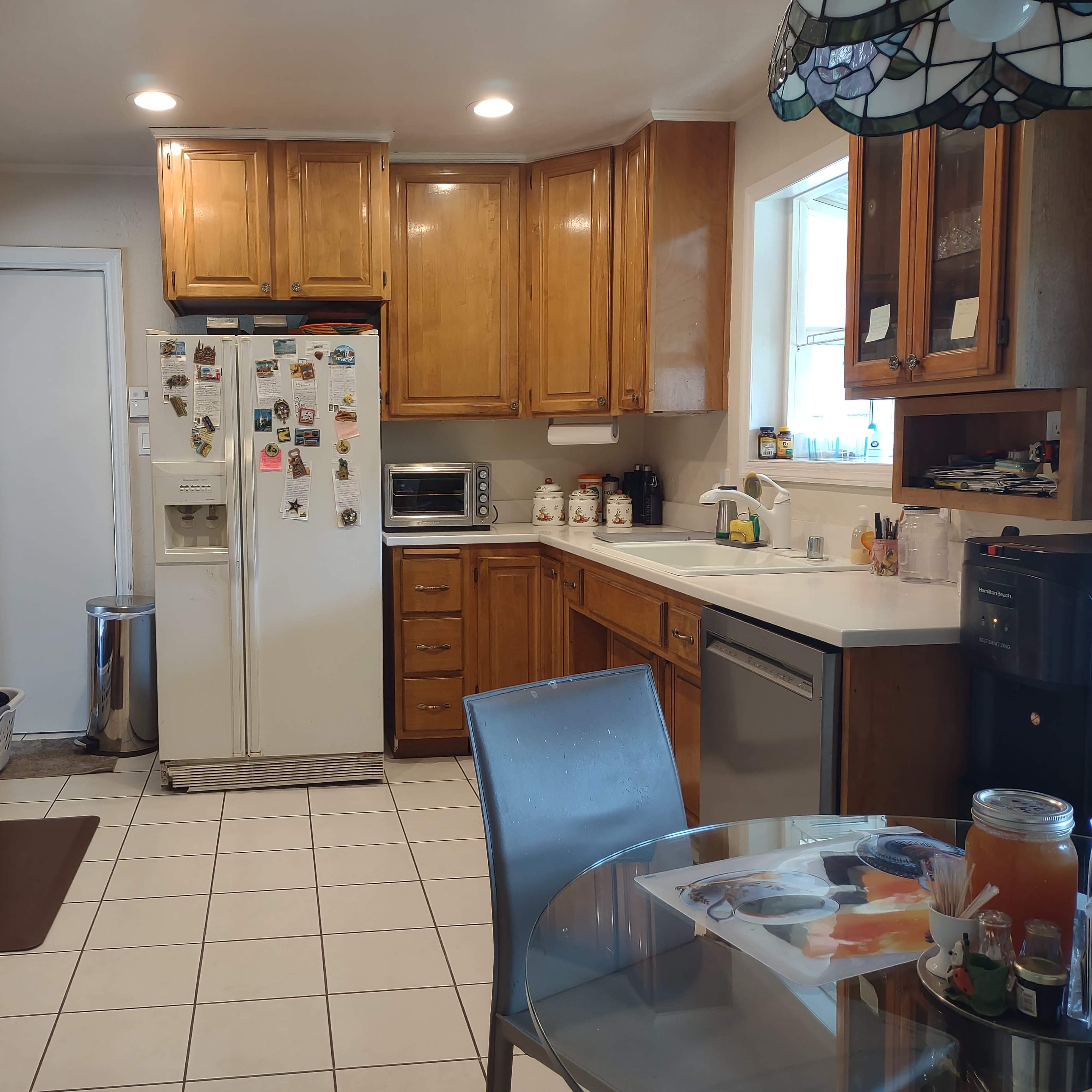 The kitchen features wooden cabinetry, white appliances, and a tiled floor with a round glass table set for dining.