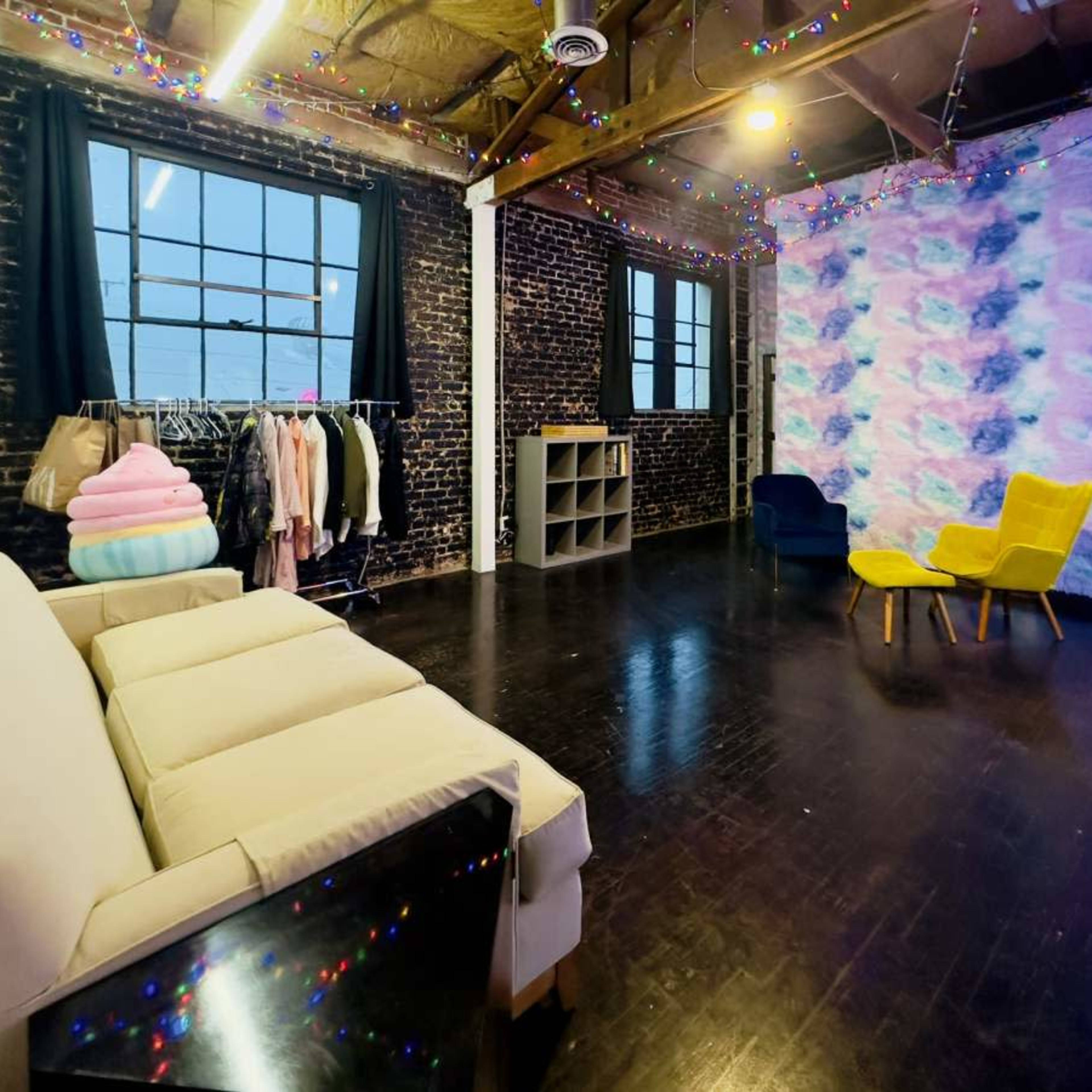 A spacious room with exposed brick walls, a sofa, two yellow chairs, a clothing rack, and decorative lights.