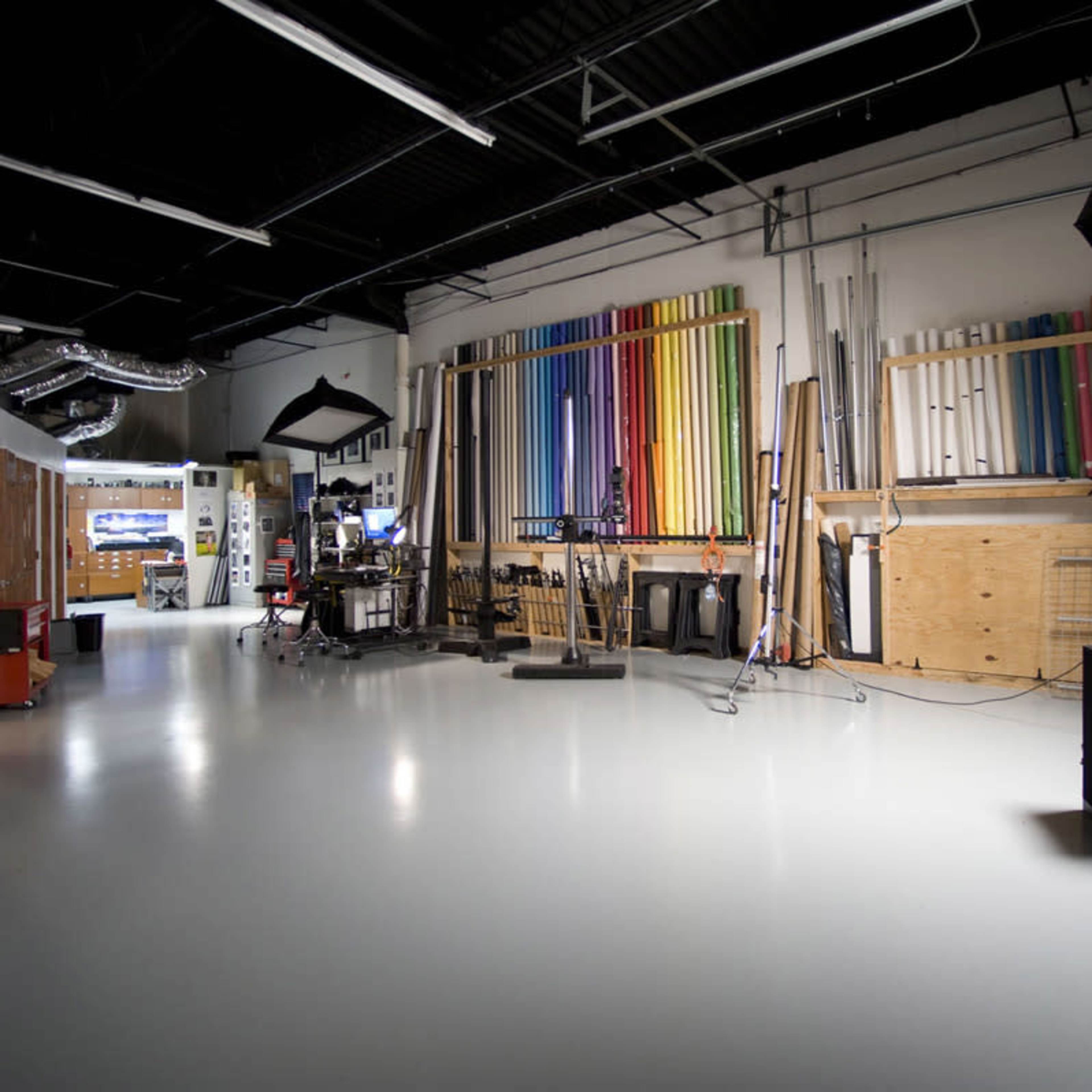 A spacious studio with various colorful backdrops neatly organized on shelves along one wall and photography equipment positioned in the center.