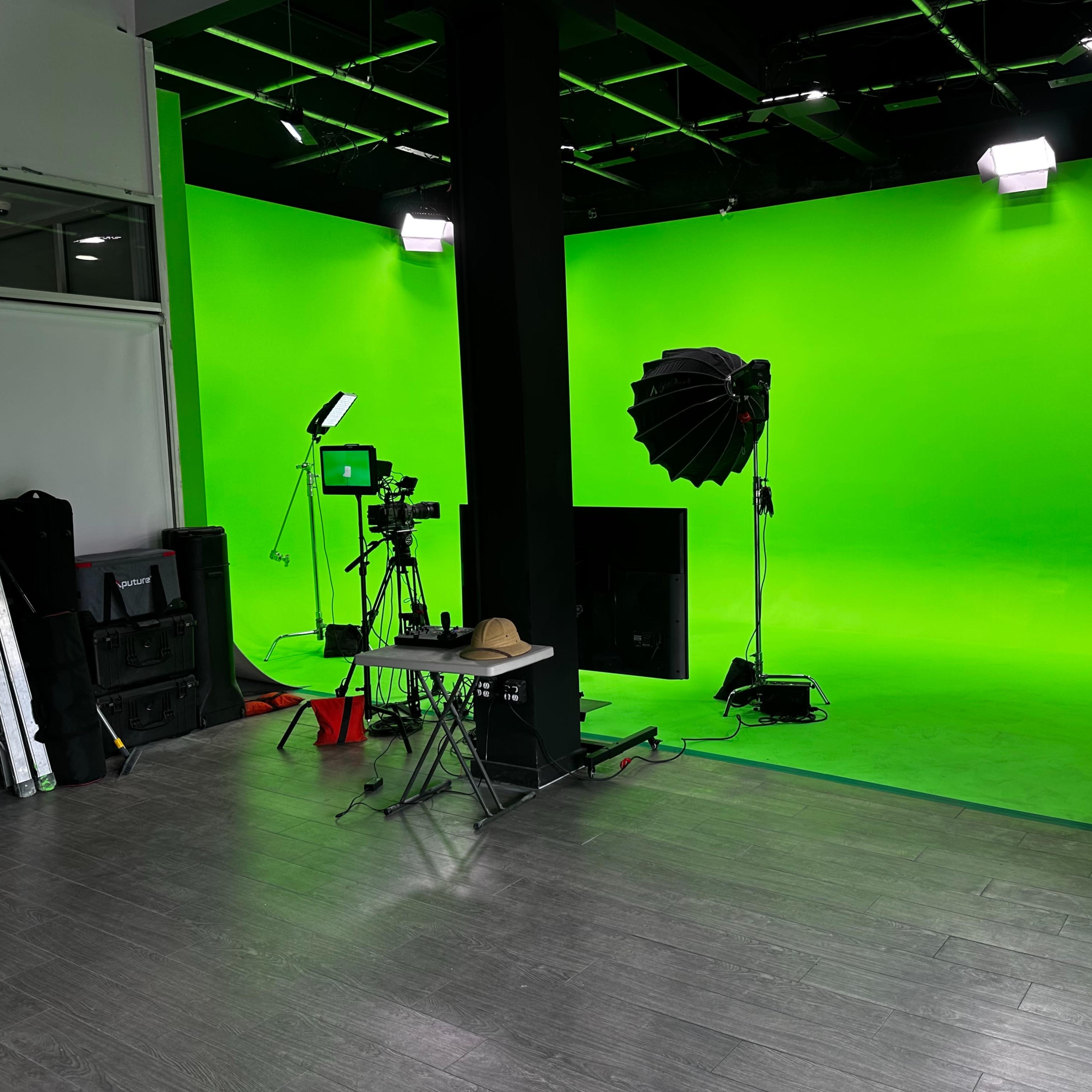 A green screen studio setup with lighting and camera equipment arranged in an empty space.