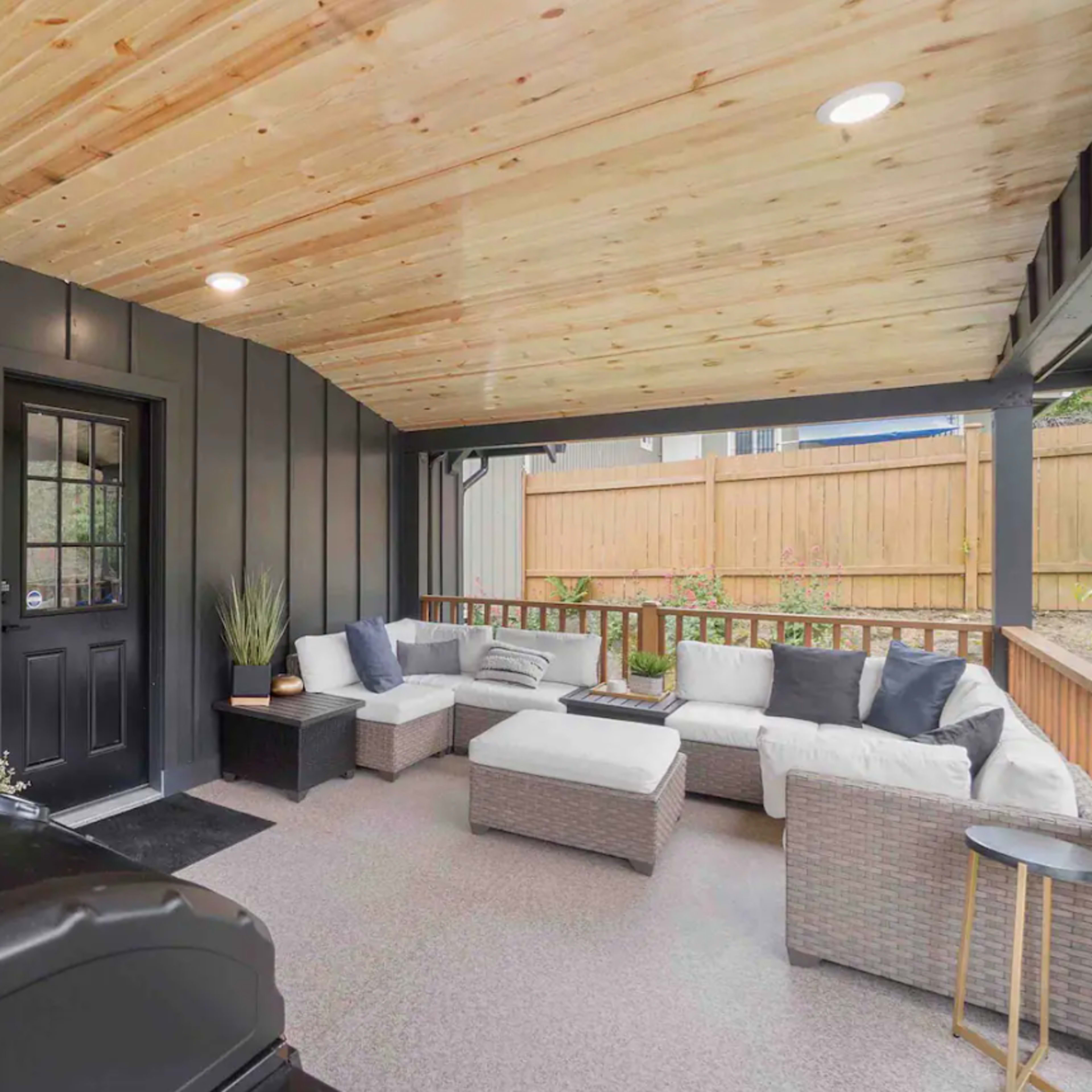 A covered patio with a seating area featuring a sofa and coffee table, alongside a grill.