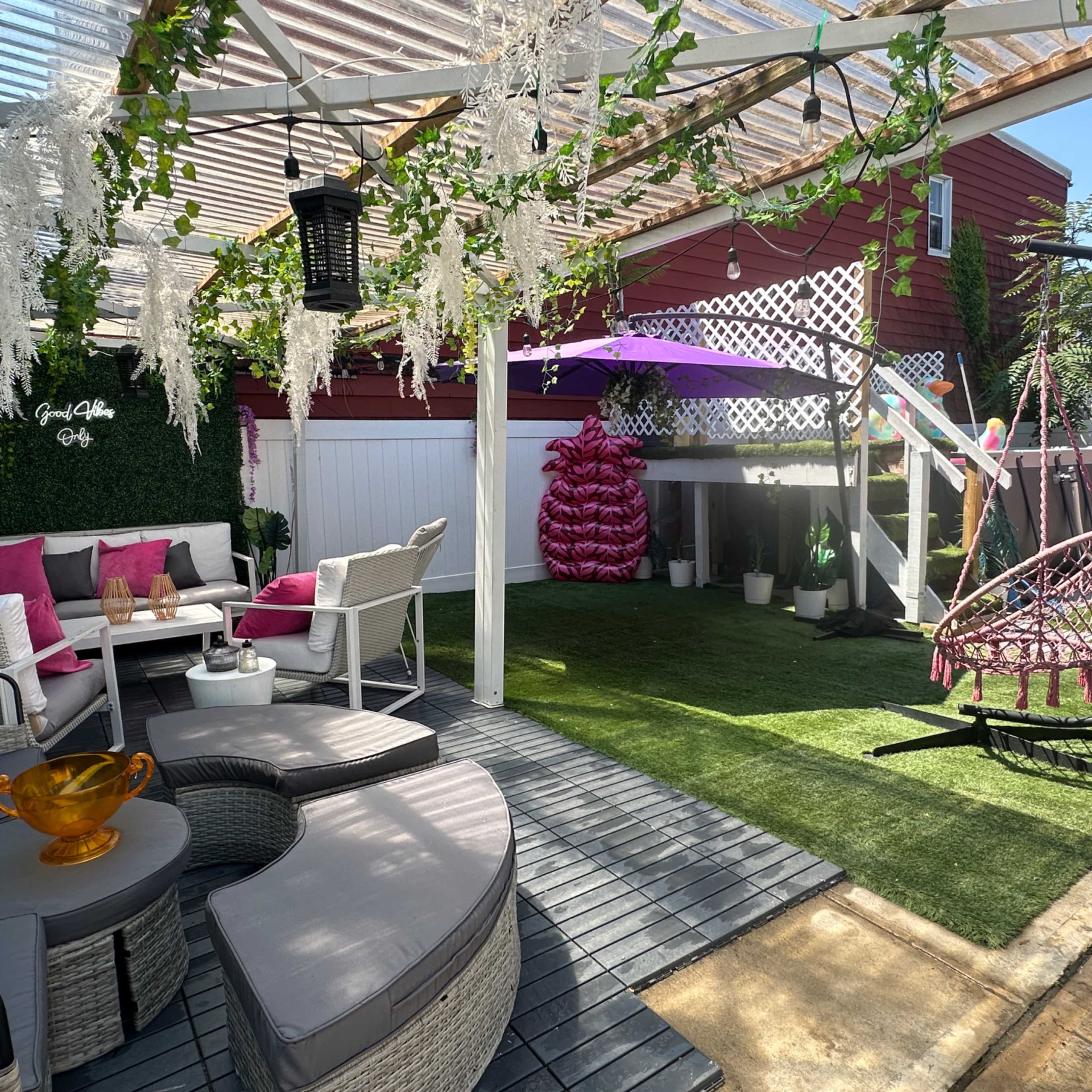 A landscaped backyard patio with seating arrangements, a swing chair, decorative plants, and a shaded area covered by a pergola.