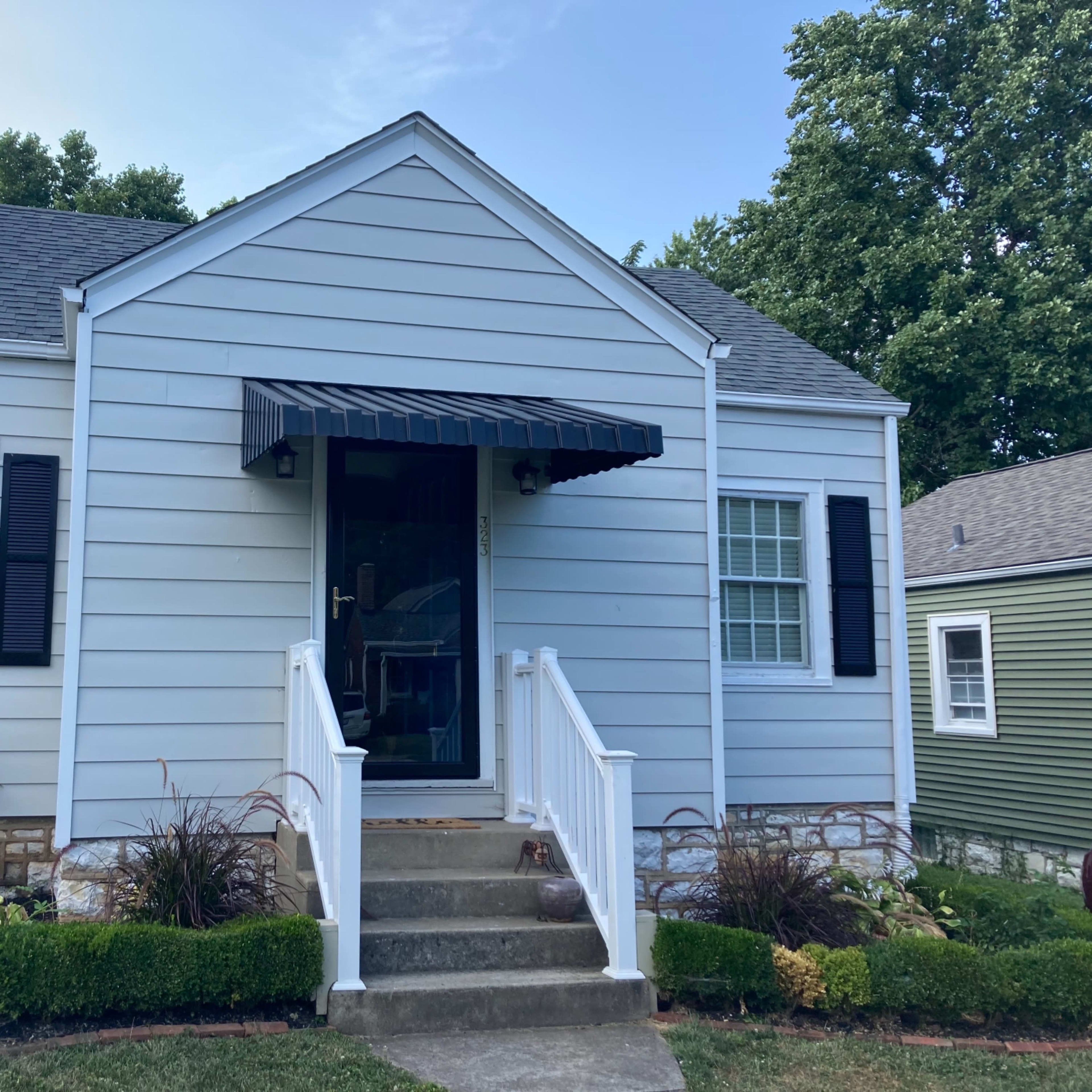A blue, single-story house with a front porch, white railings, and black shutters.
