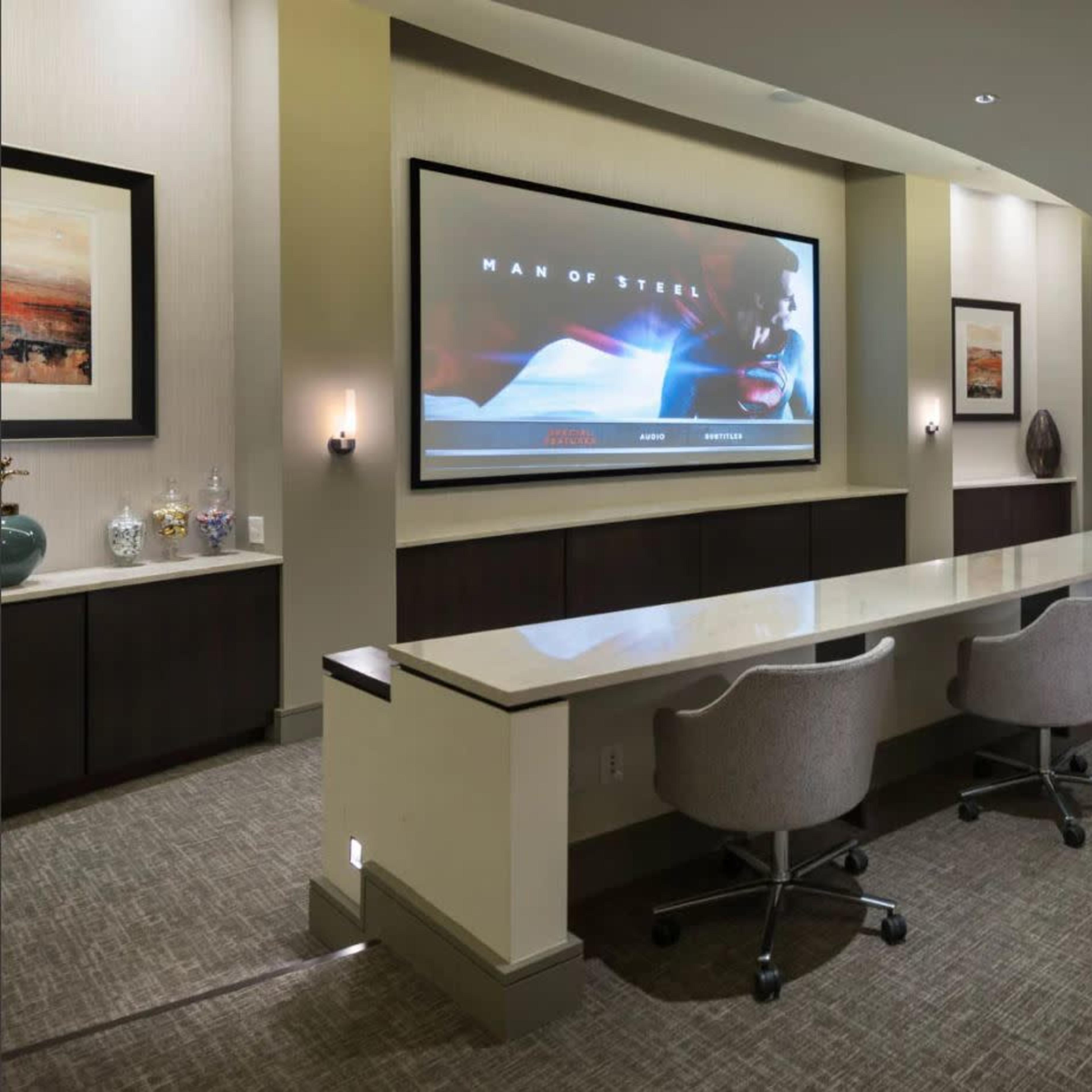 A conference room with a large screen displaying a scene from "Man of Steel" and a long table surrounded by rolling chairs.
