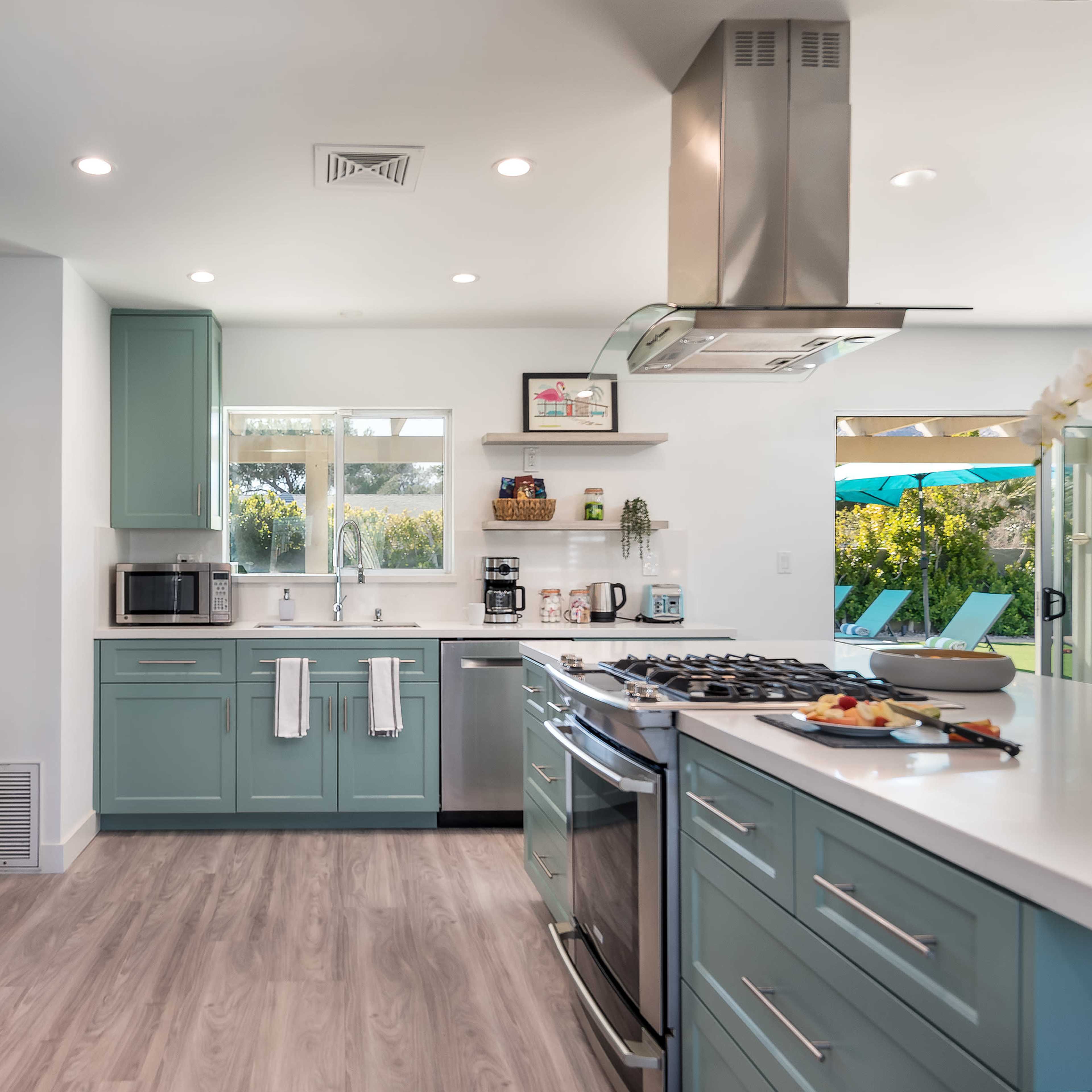 A modern kitchen features teal cabinetry, stainless steel appliances, and a centered island with a gas stove.