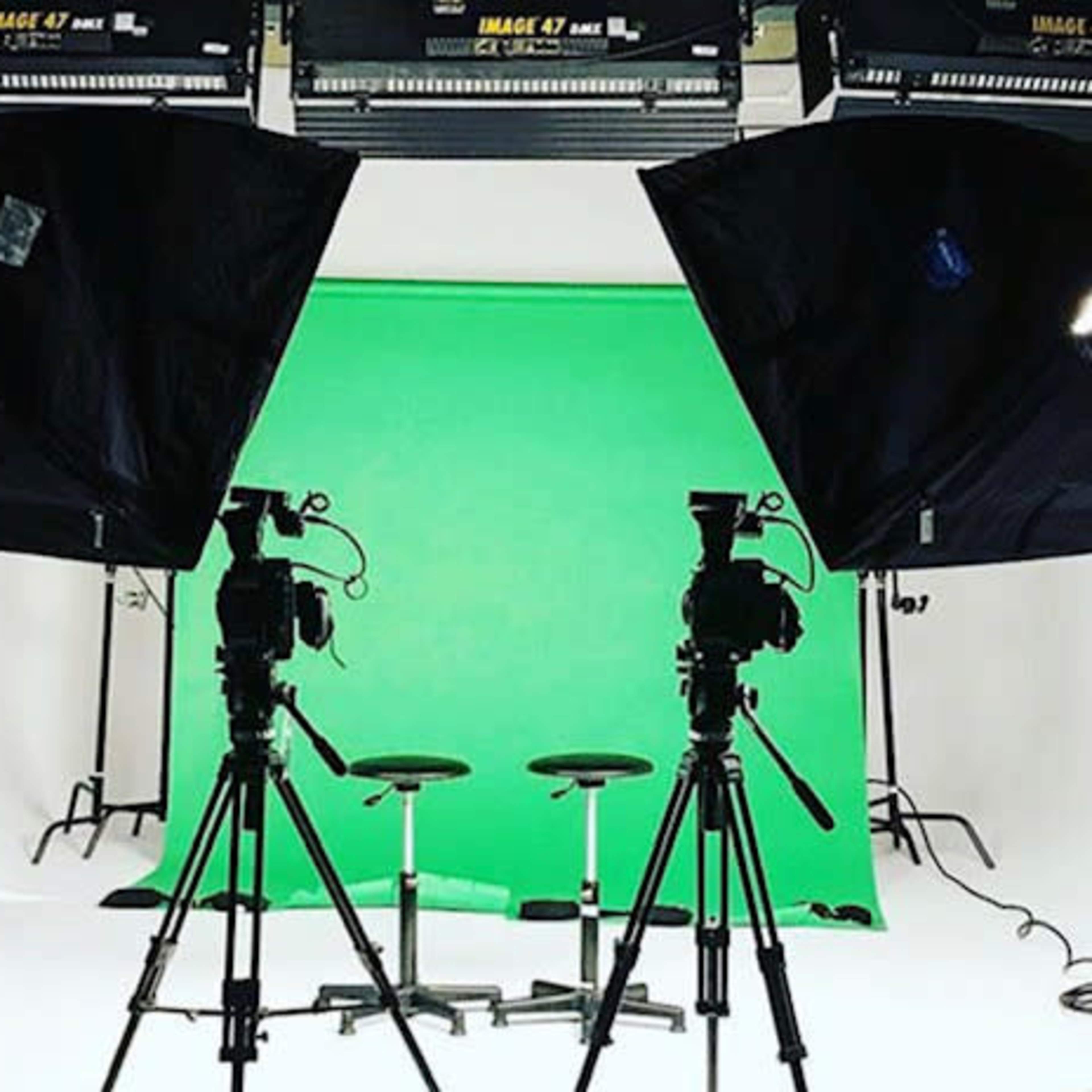 A photography studio setup with two cameras facing two black stools against a green backdrop, illuminated by softbox lights.