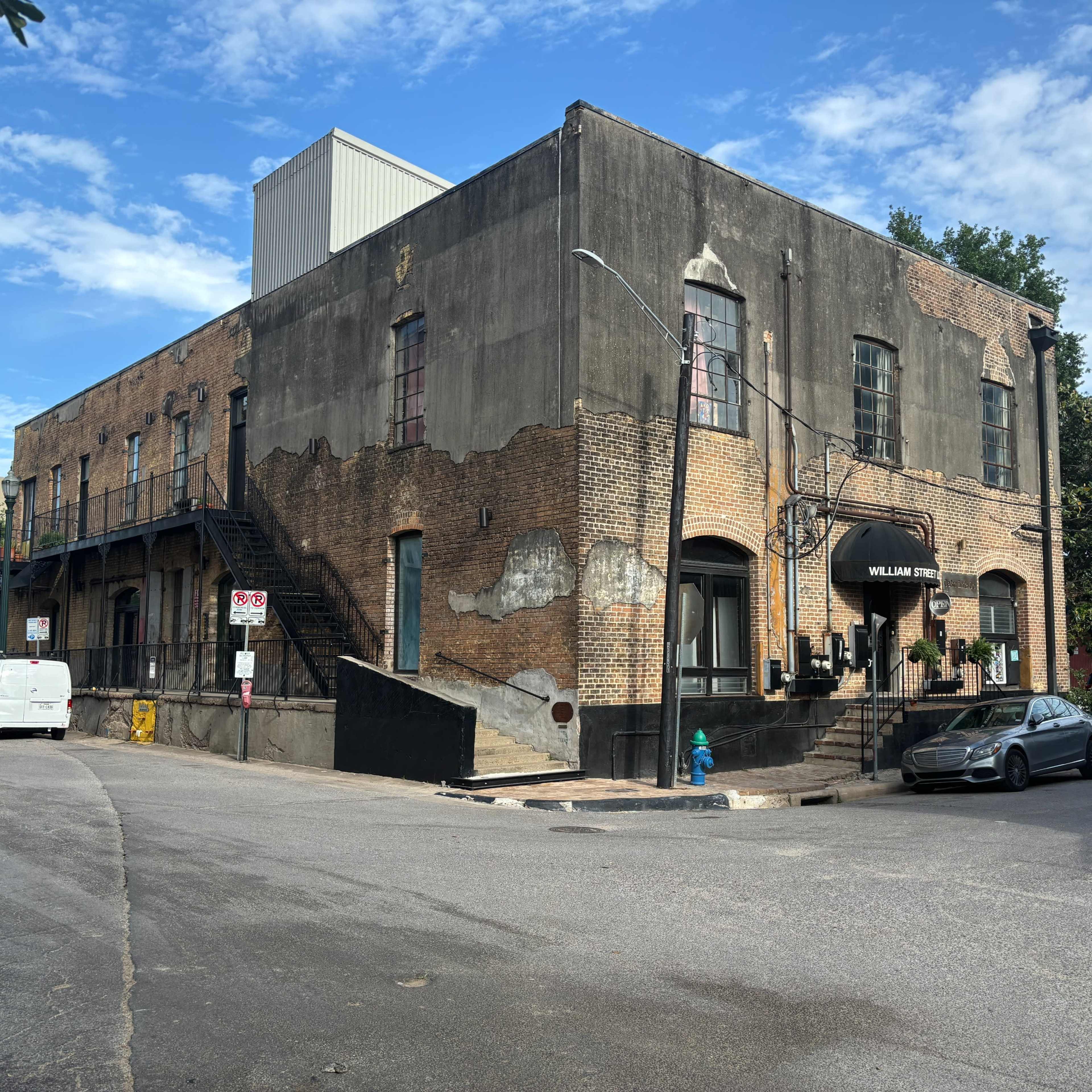 An old brick building with a weathered exterior, located at the corner of a street, featuring a staircase and a canopy entrance.