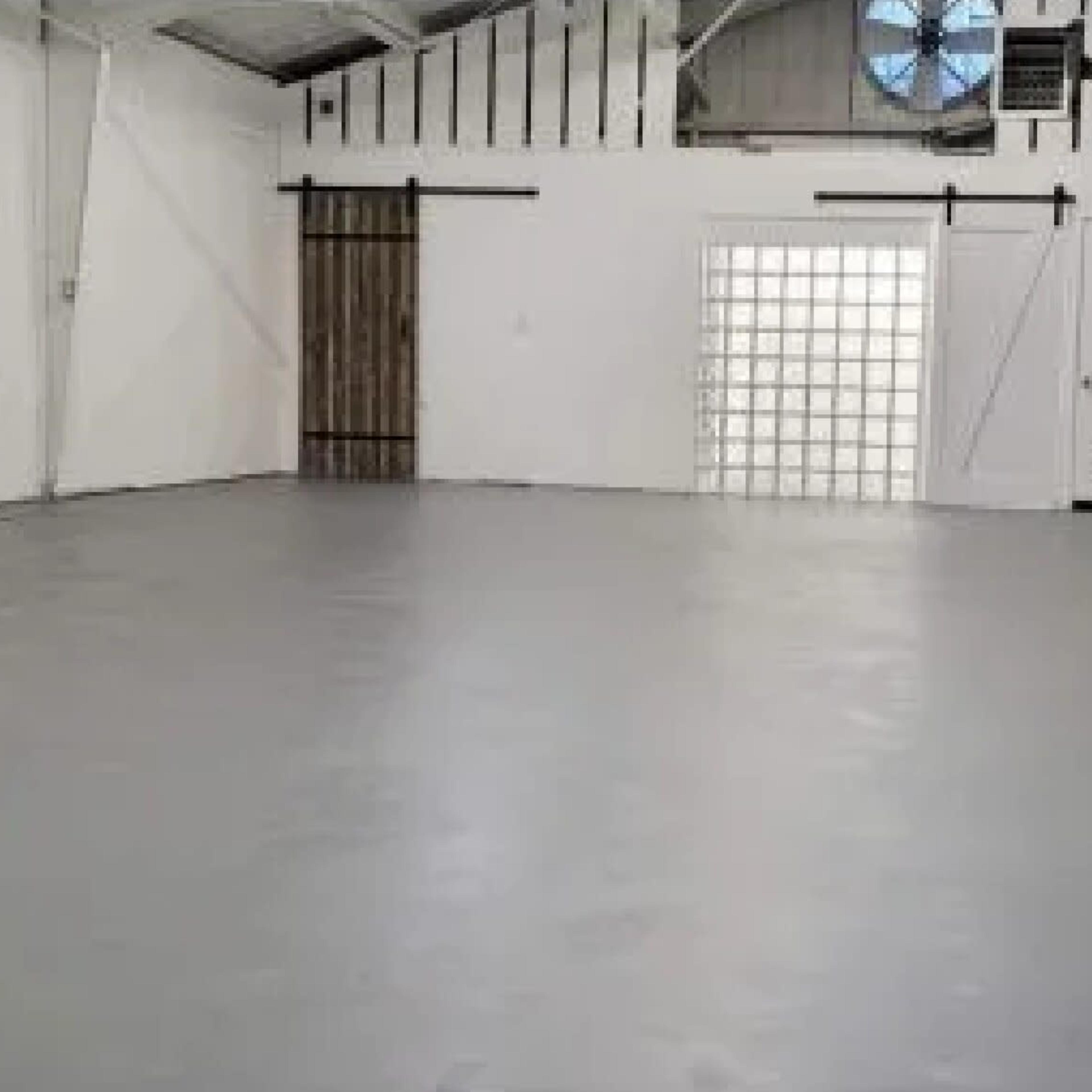 An empty, well-lit interior space with gray flooring and white walls, featuring a large window and a door.