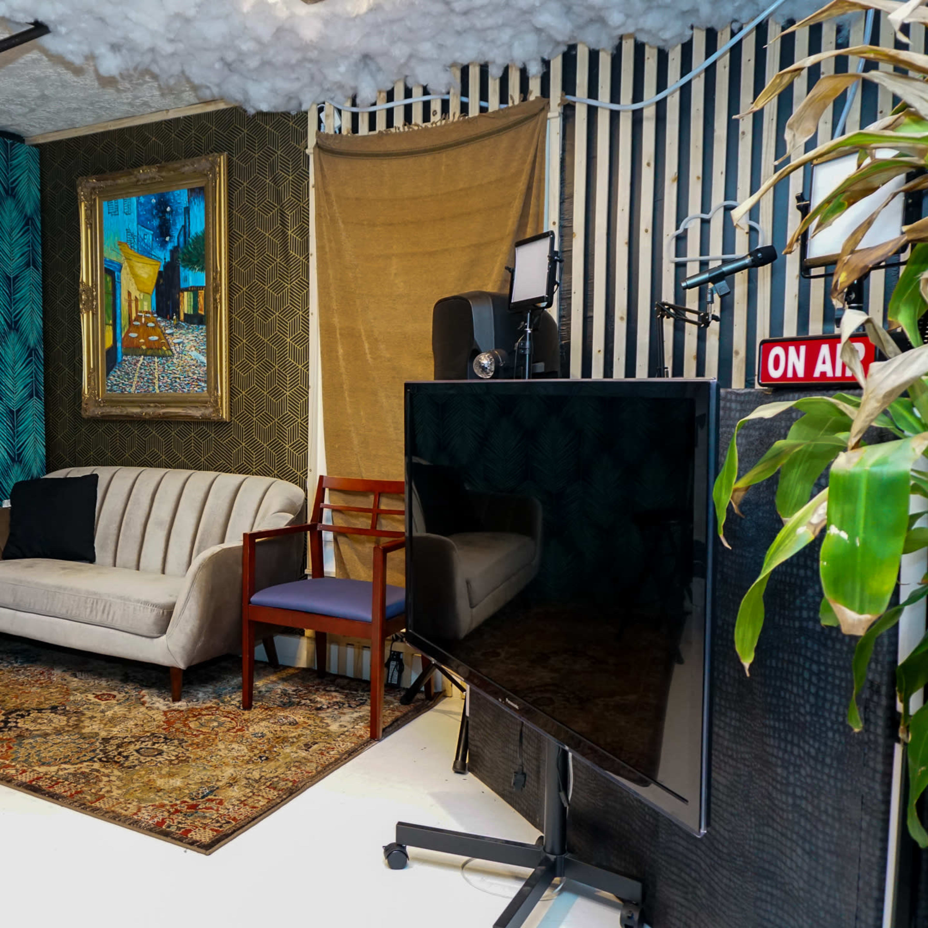 A cozy recording studio featuring a striped wall, a painting, a patterned rug, a sofa, a chair, and a large television.