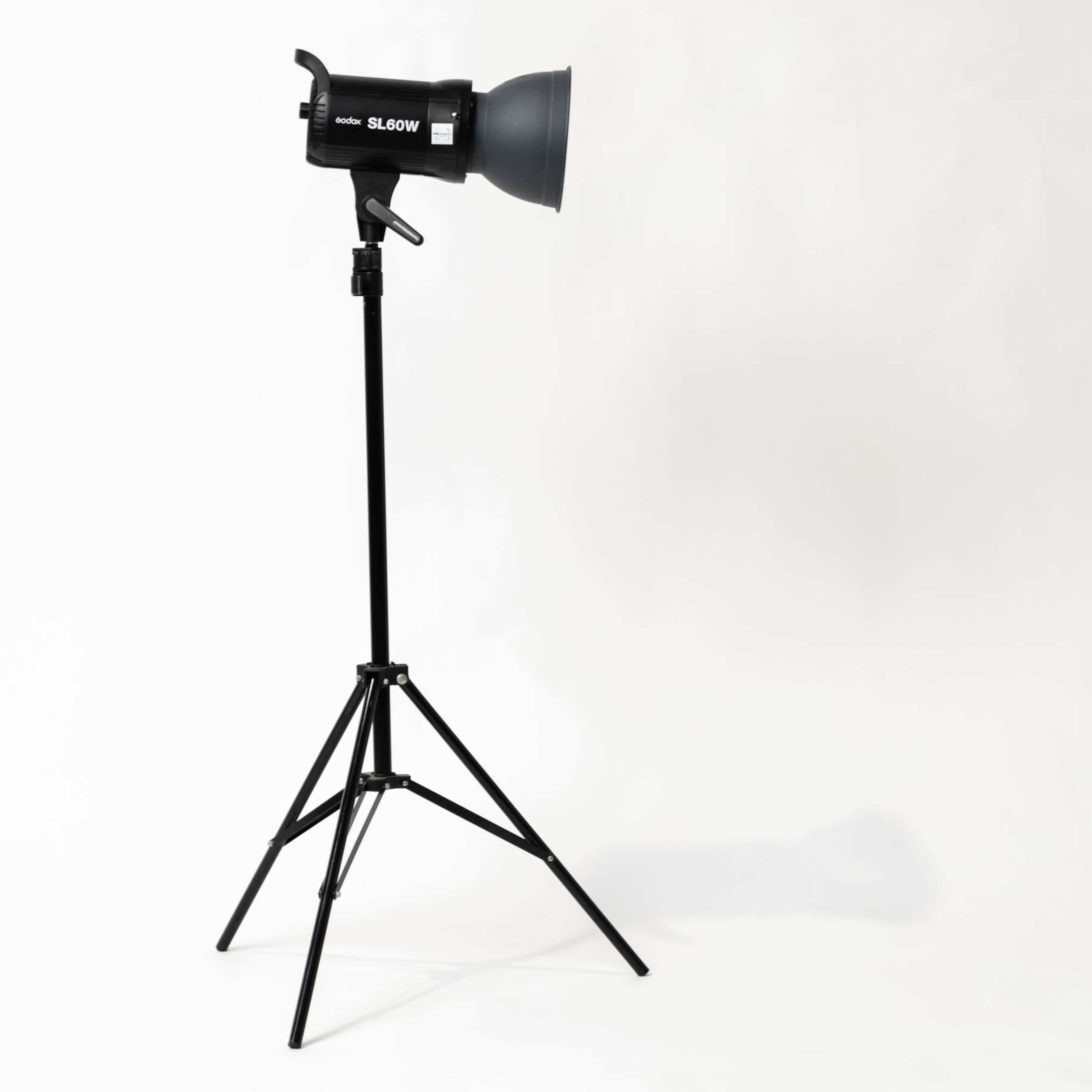 A black studio light on an adjustable tripod stand is positioned against a plain white background.