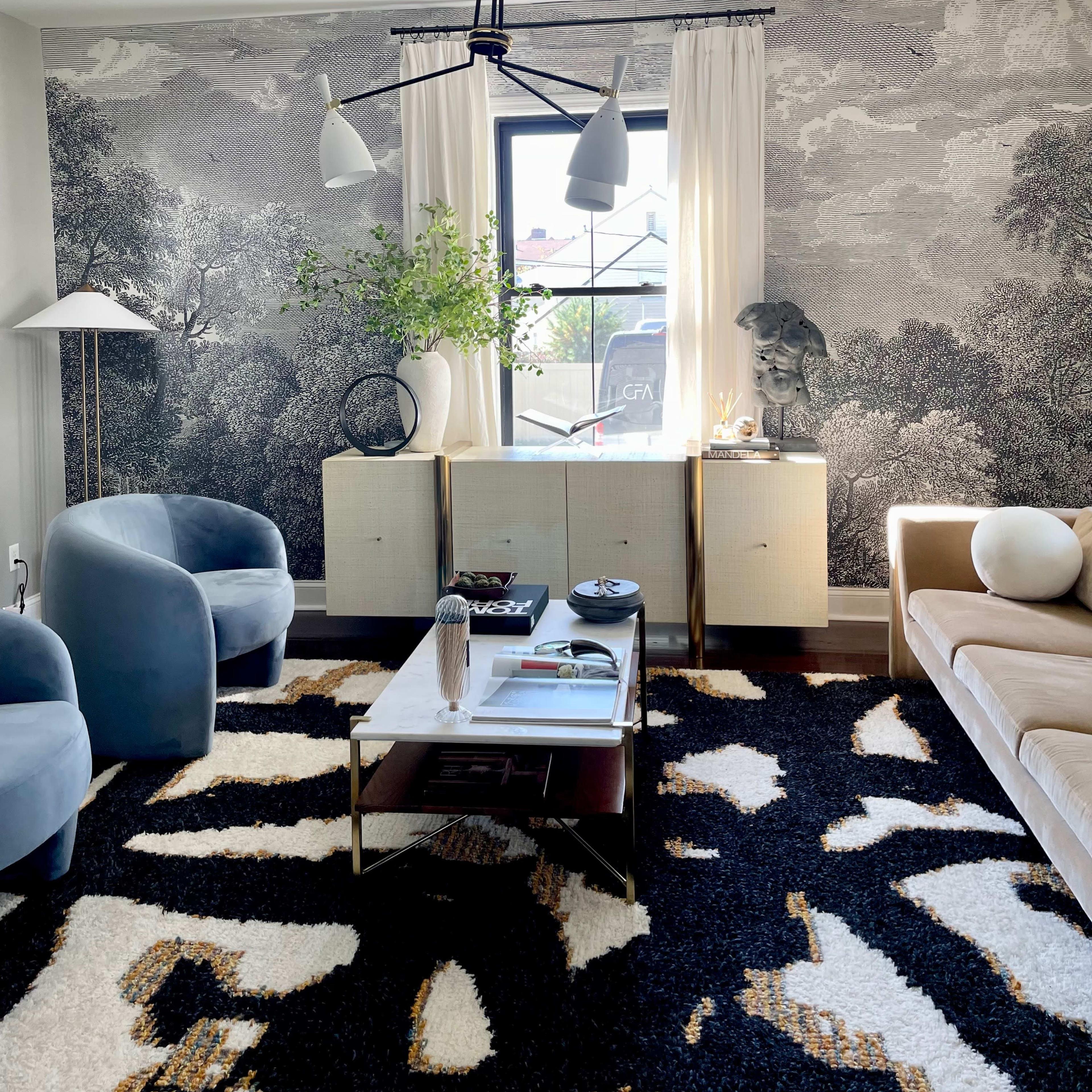 A modern living room featuring a patterned rug, a coffee table, a light fixture, and a large mural on the wall.