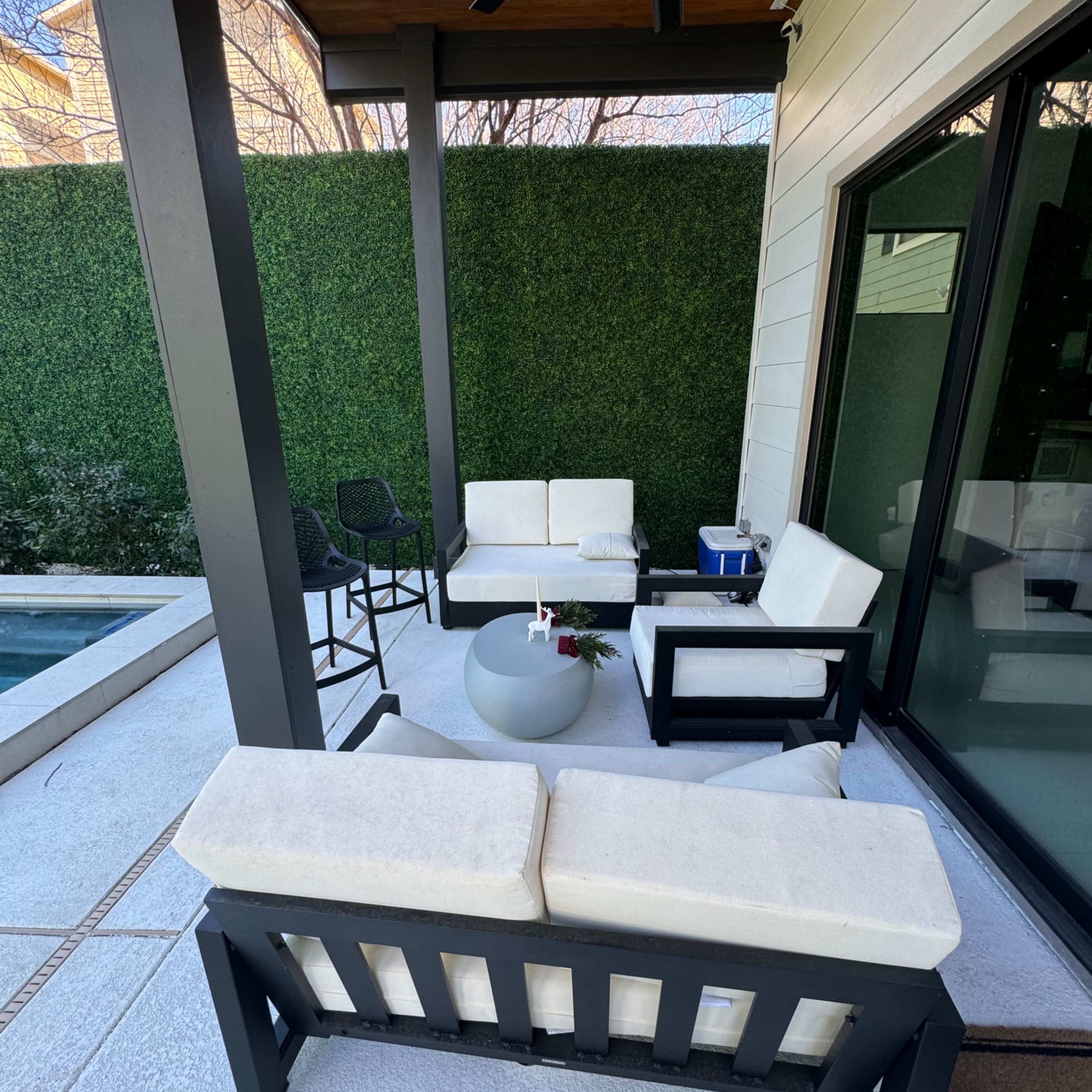 A covered outdoor seating area features a circular table surrounded by modern furniture and a small pool nearby.
