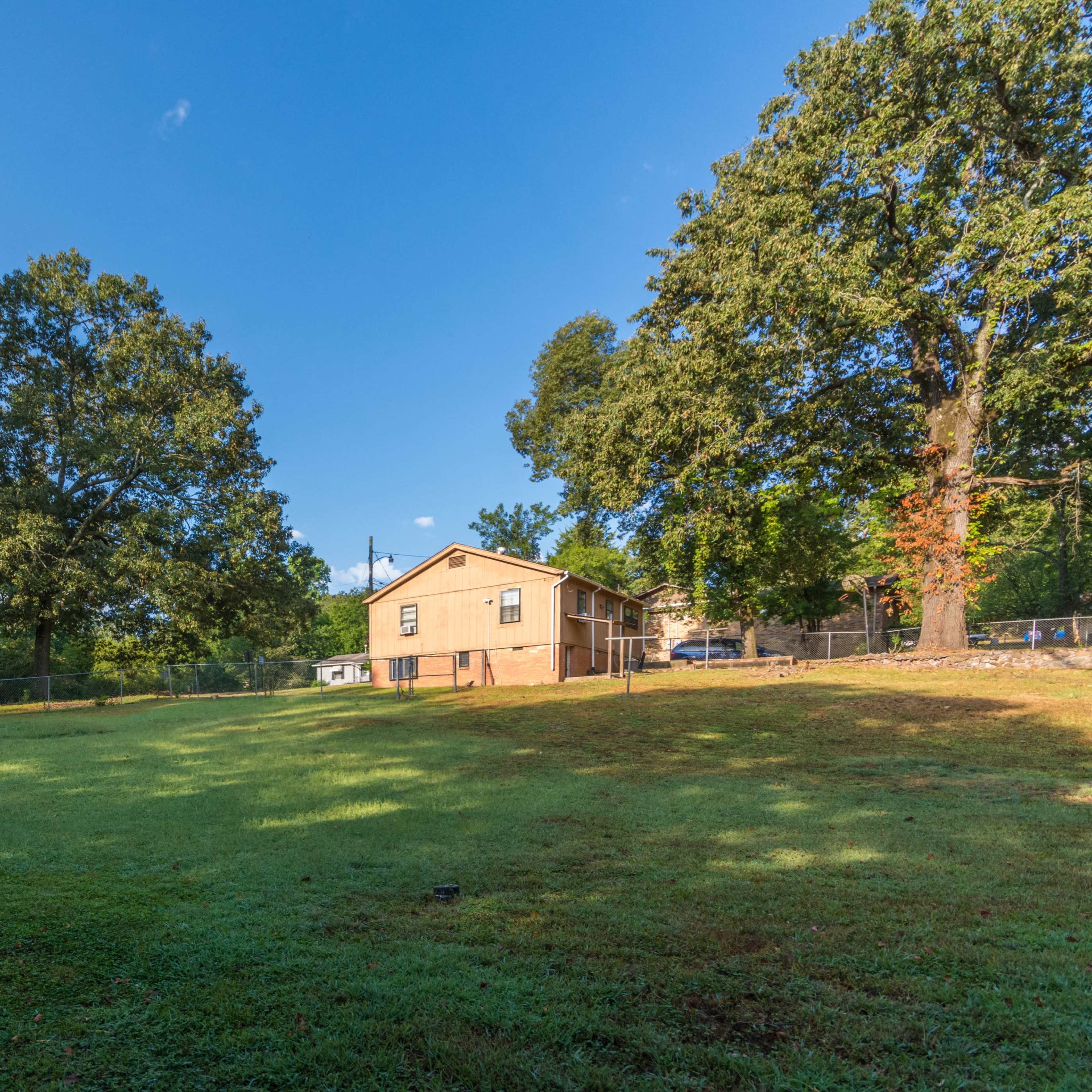 A single-story house is situated on a grassy lot surrounded by several trees.