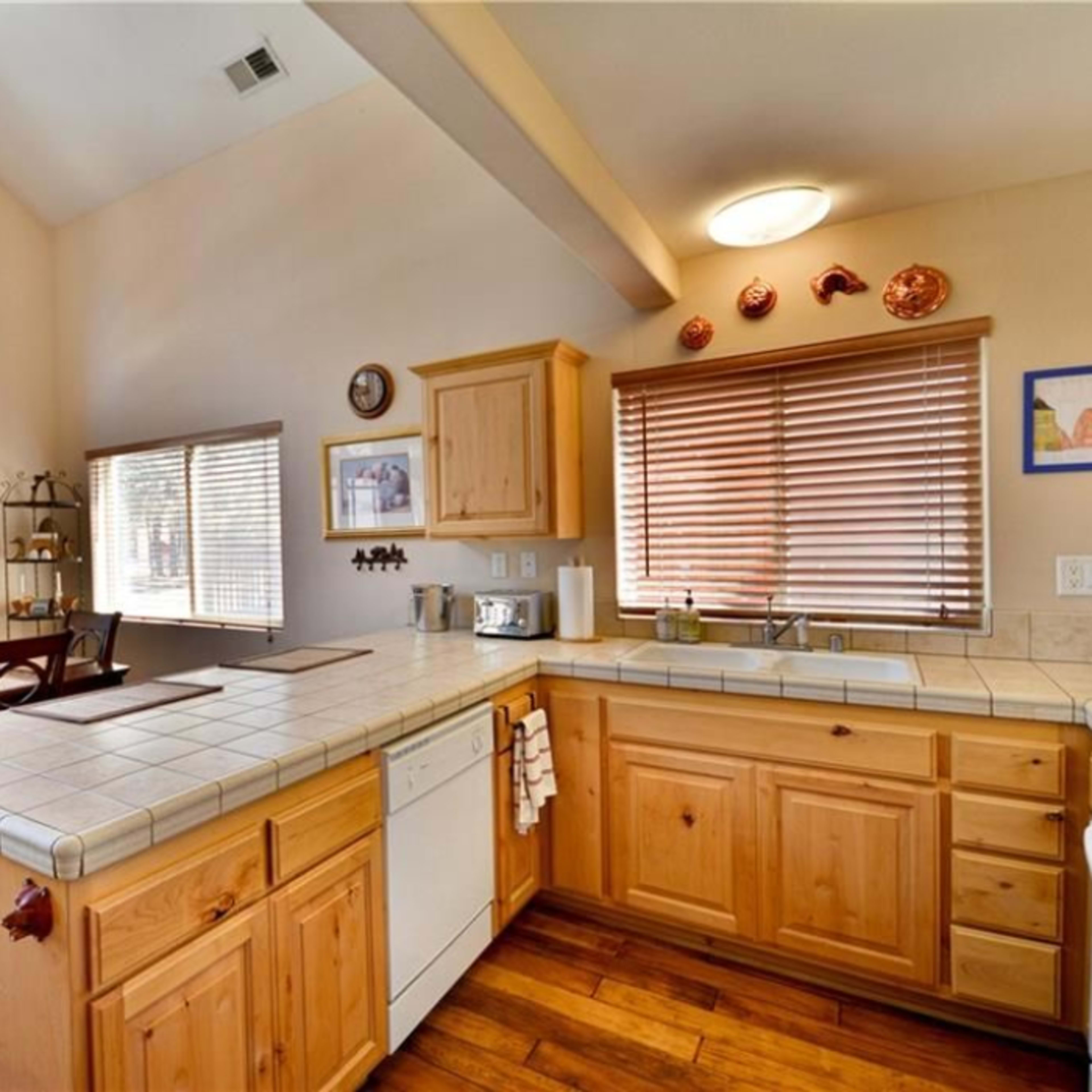 A modern kitchen with wooden cabinets, a tiled countertop, and a dining area with a wooden table and chairs.