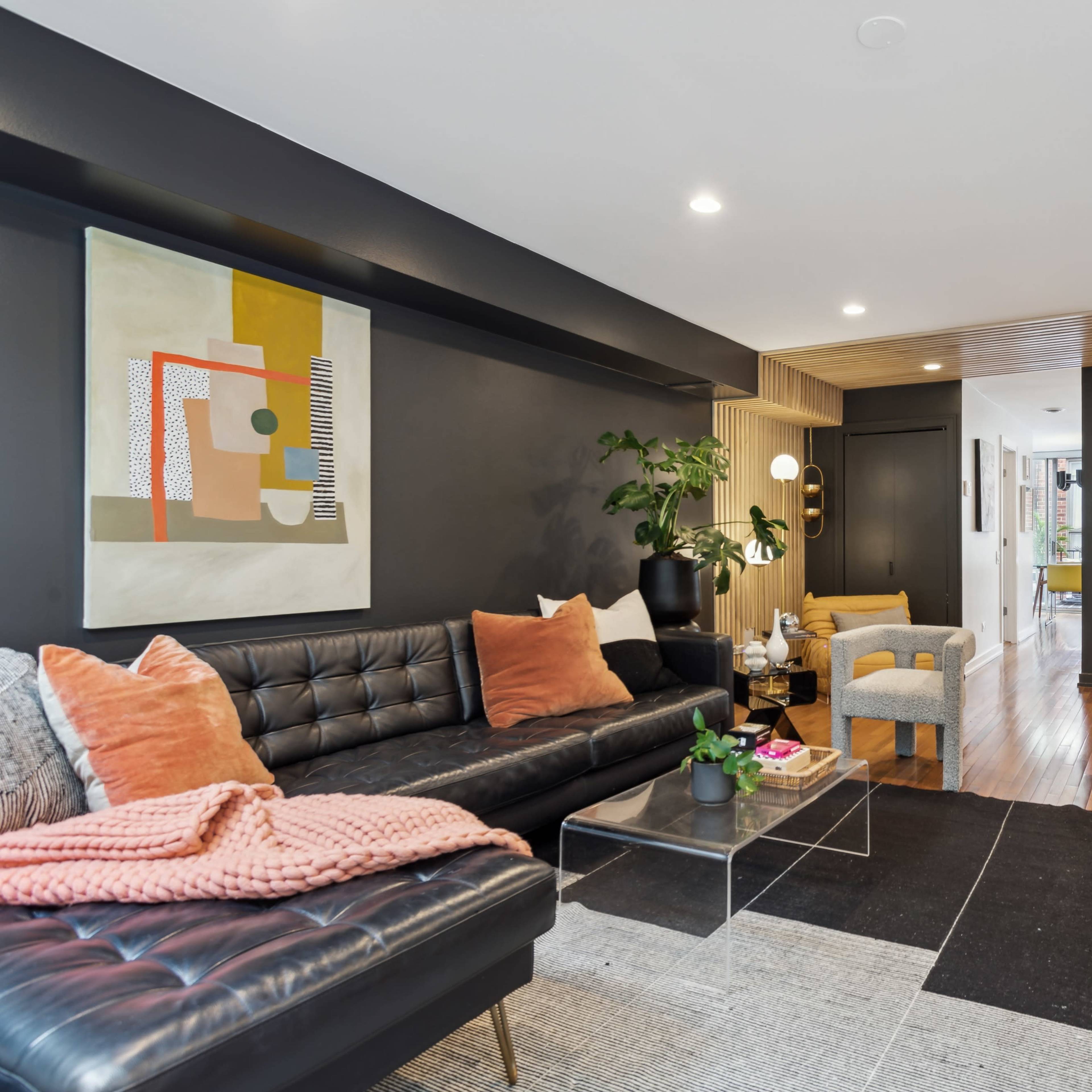 A modern living room featuring a black leather sofa with colorful pillows, a glass coffee table, and a staircase leading to an upper level.