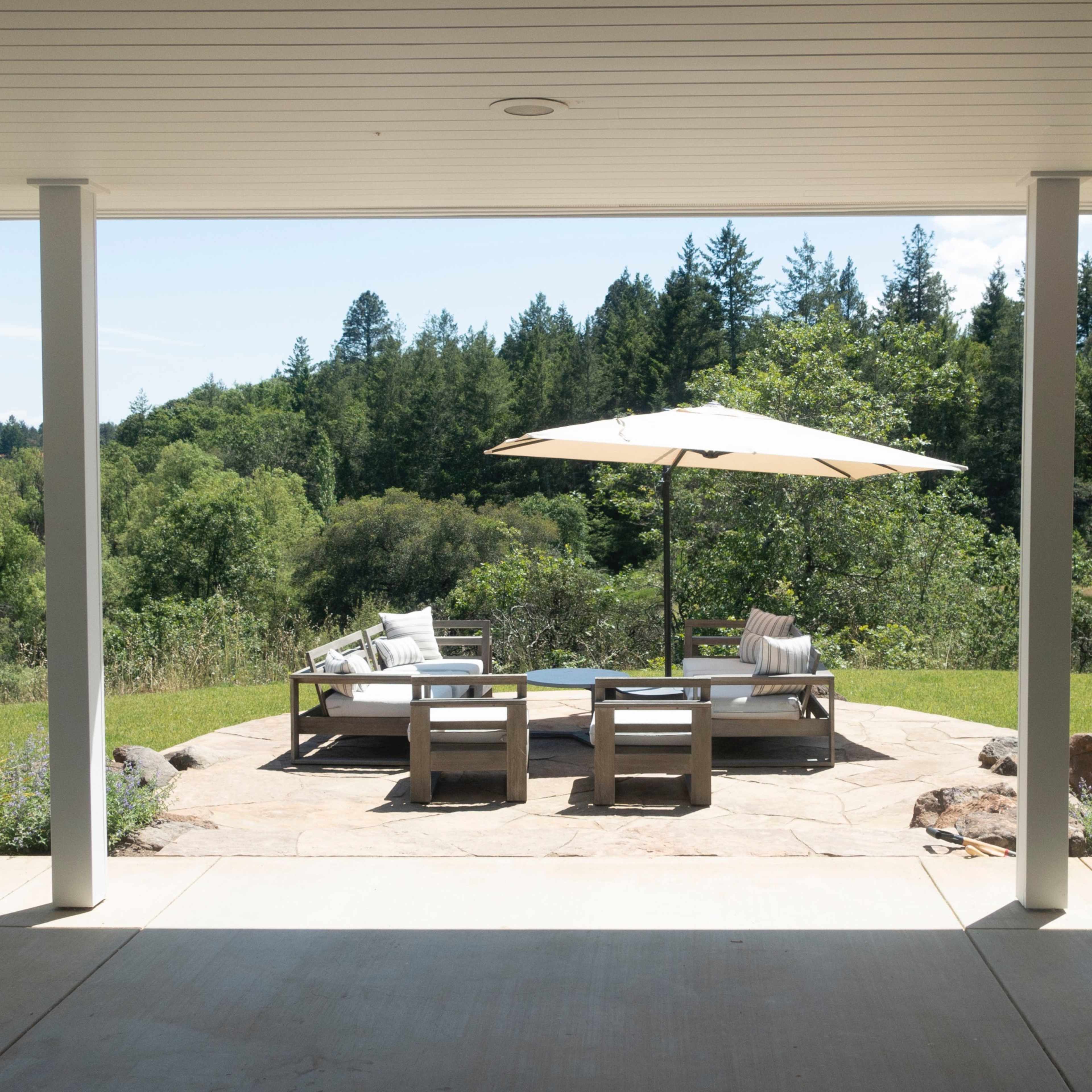 A patio with seating and an umbrella overlooks a green landscape of trees and hills.