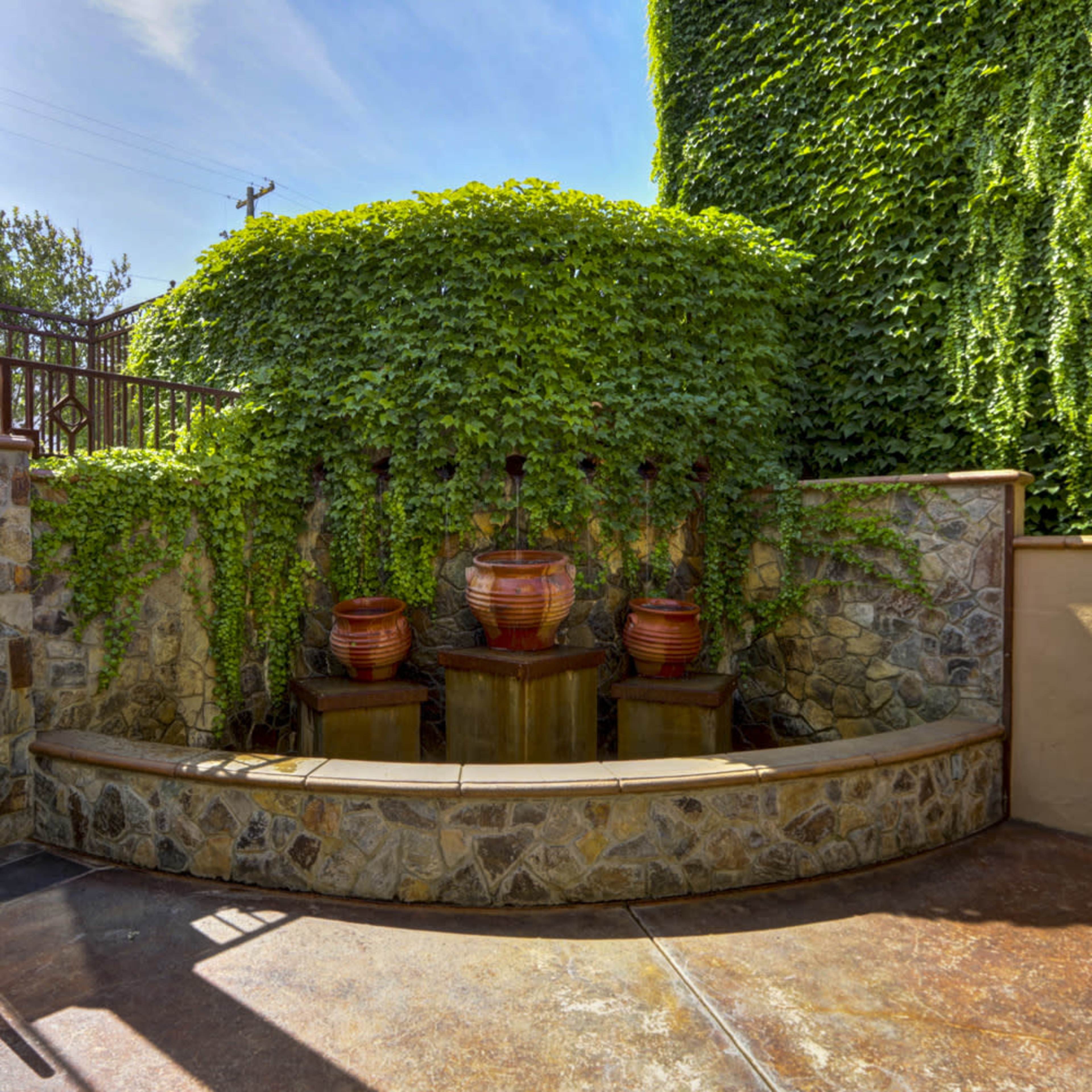 A small outdoor area featuring a stone wall with three water fountains and lush green ivy cascading over the top.