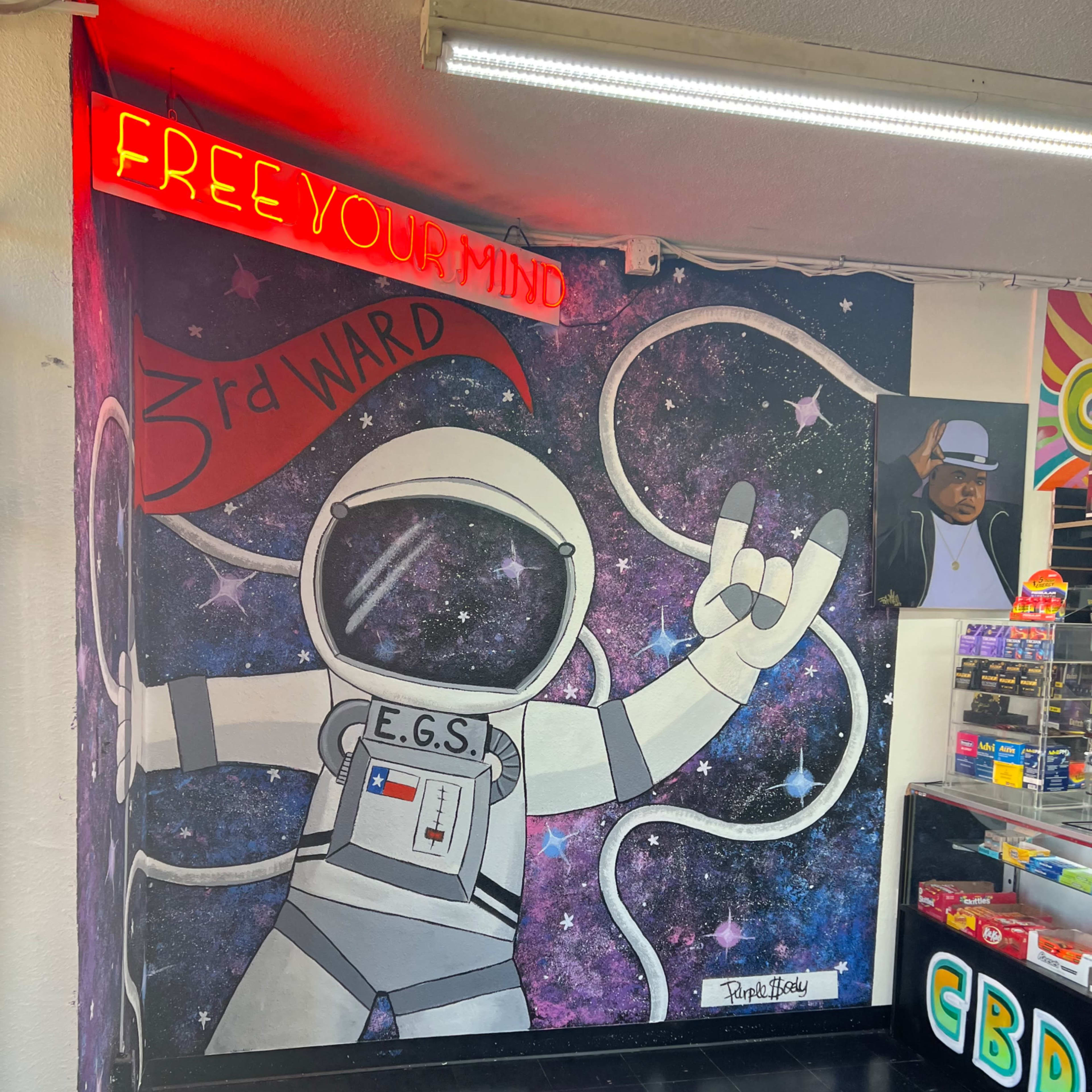 A mural of an astronaut with the text "3rd WARD" and "FREE YOUR MIND" in a colorful galaxy background on a wall inside a shop.