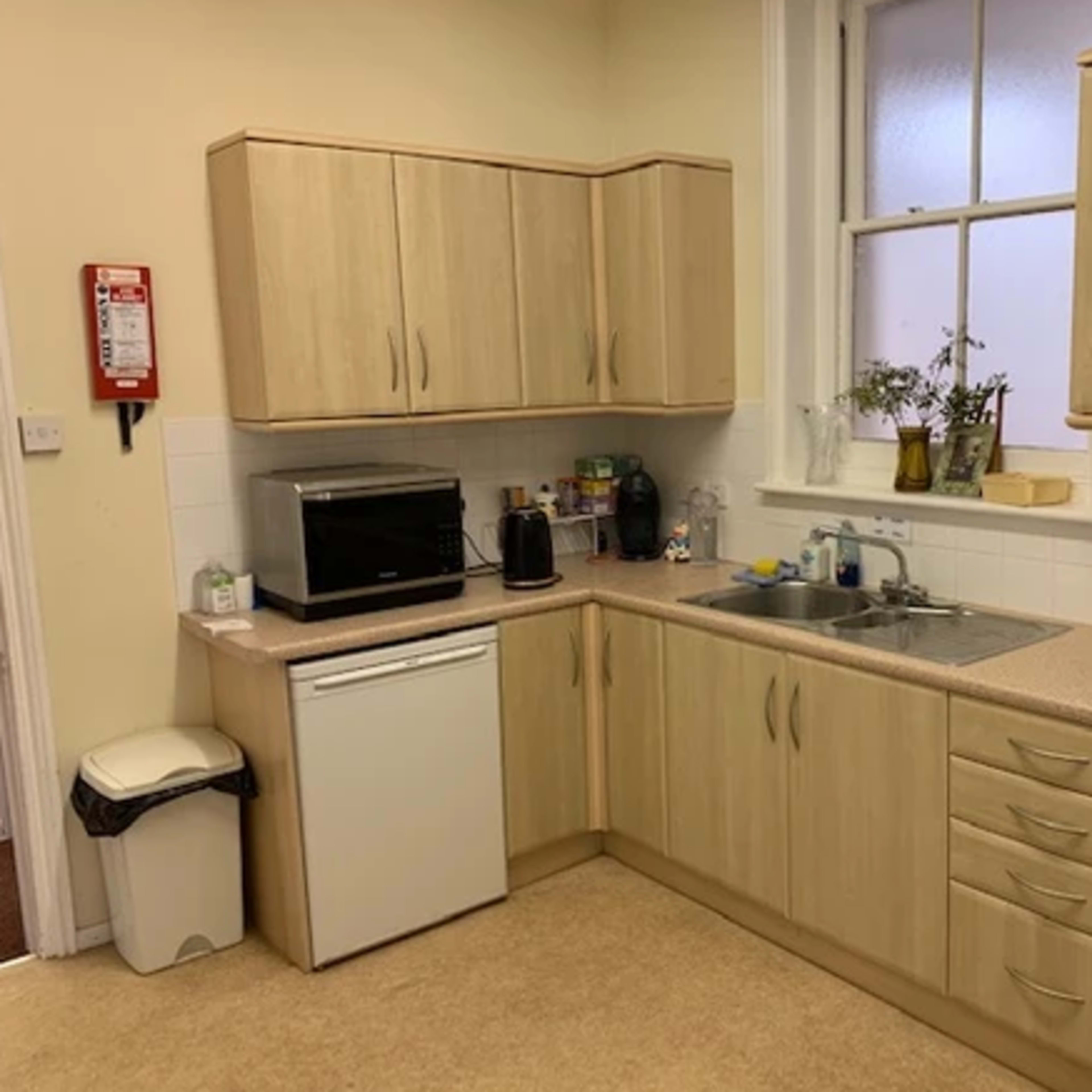 A kitchen with wooden cabinets, a sink, a microwave, a kettle, a dishwasher, and a stove.