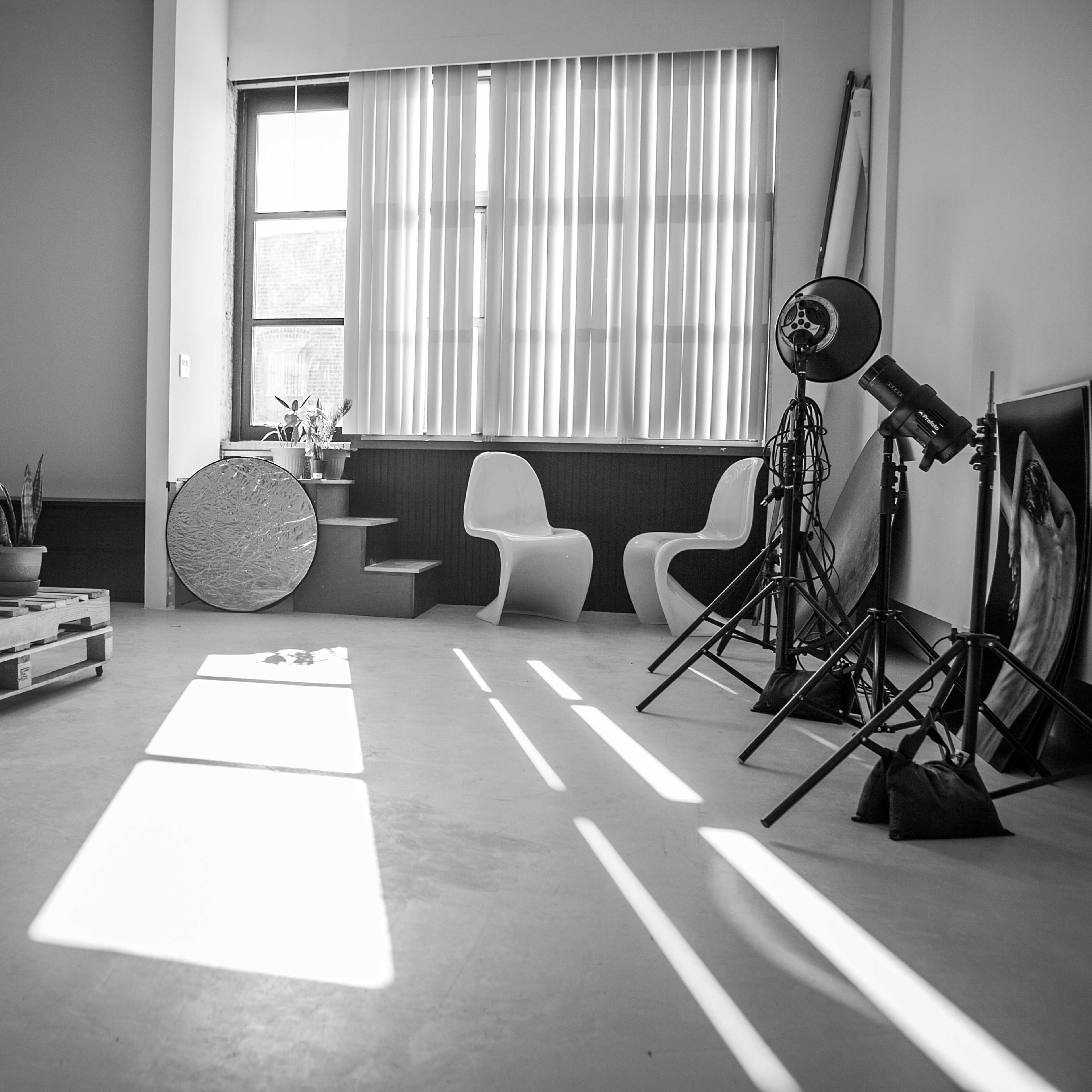 A minimalist interior space with a wooden pallet sofa, two modern chairs, a circular table, and photography lighting equipment.