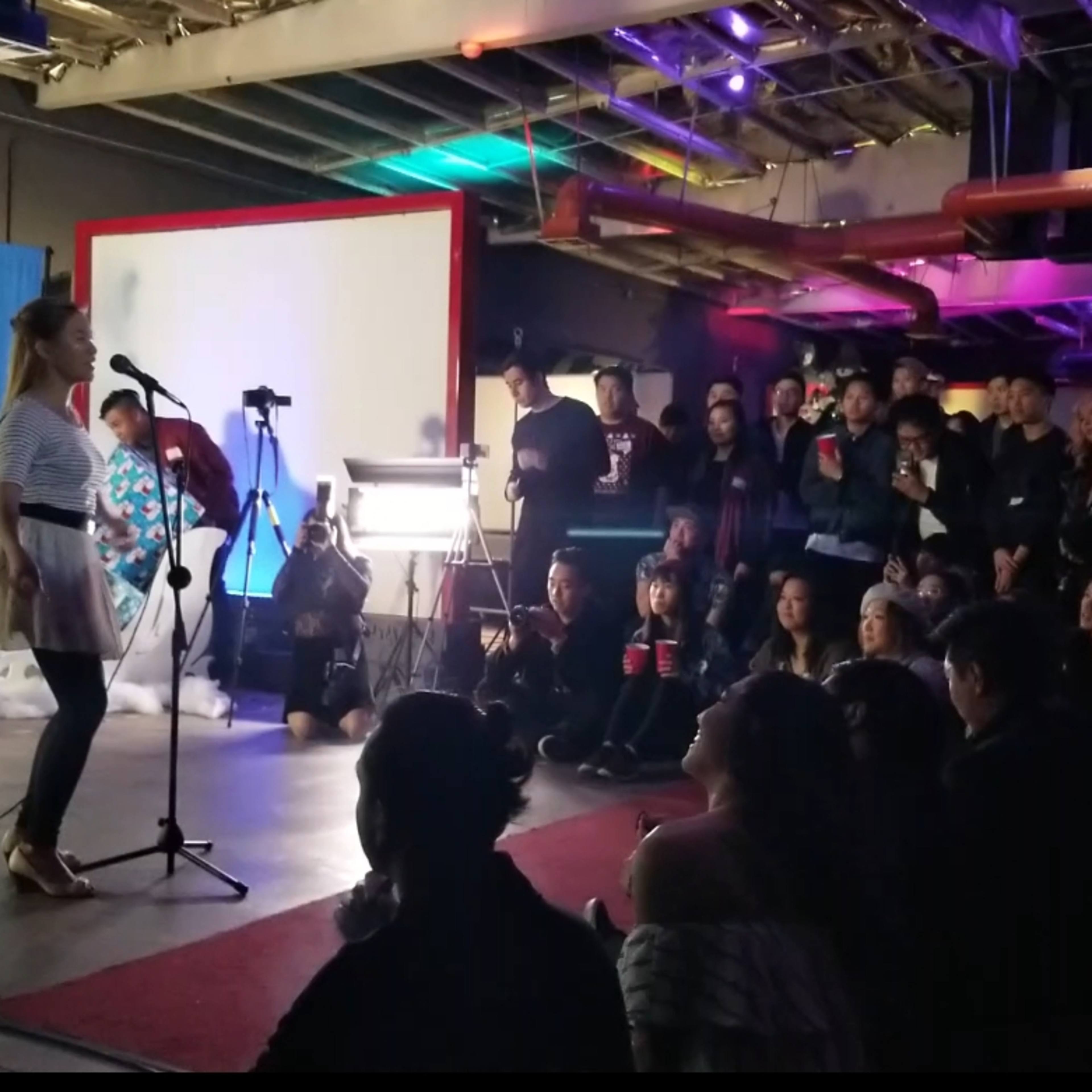 A singer performs on stage in front of an audience seated on the floor, with a decorated backdrop of white trees and deer.