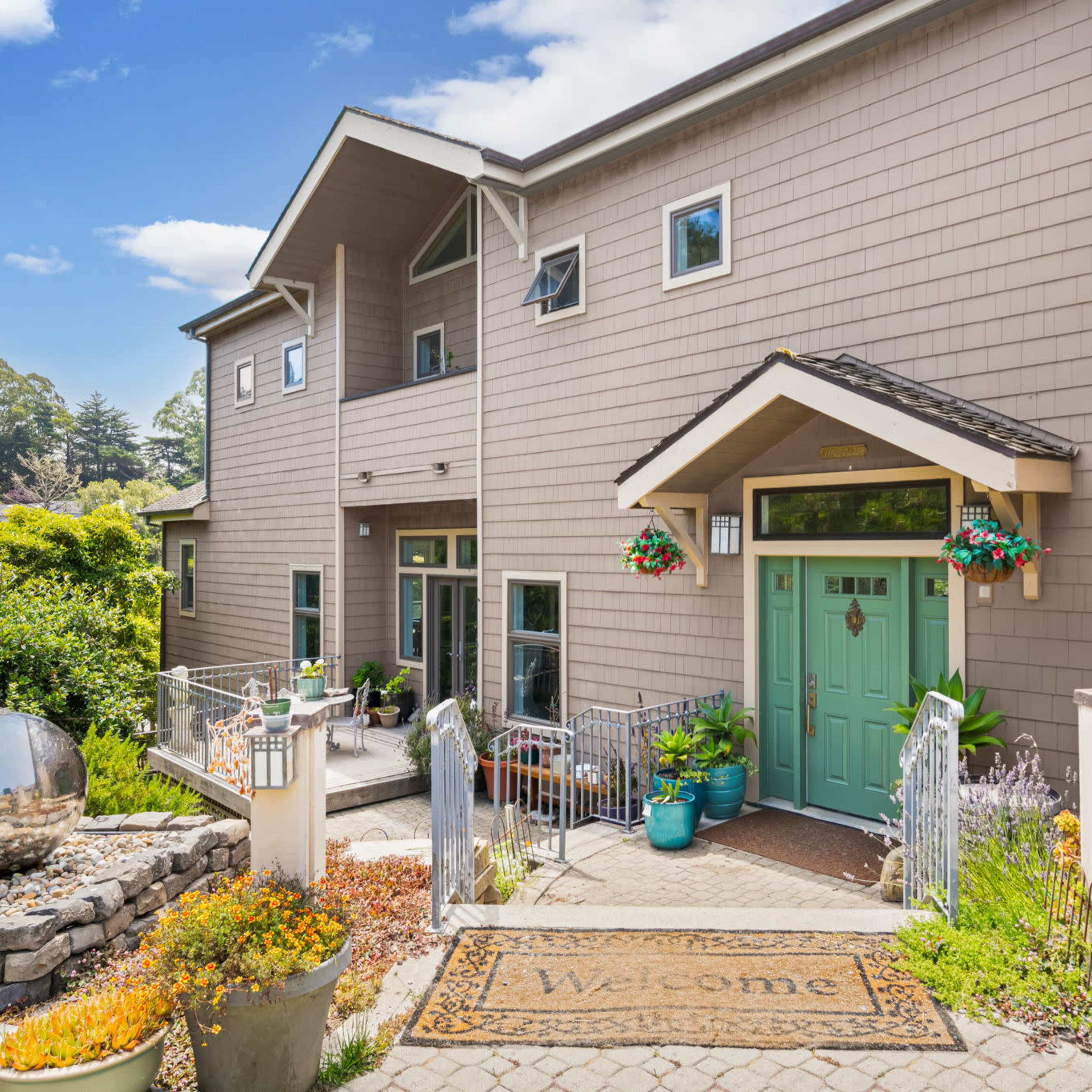 A two-story house with a welcoming entrance, featuring double front doors, potted plants, and a decorative stone pathway.