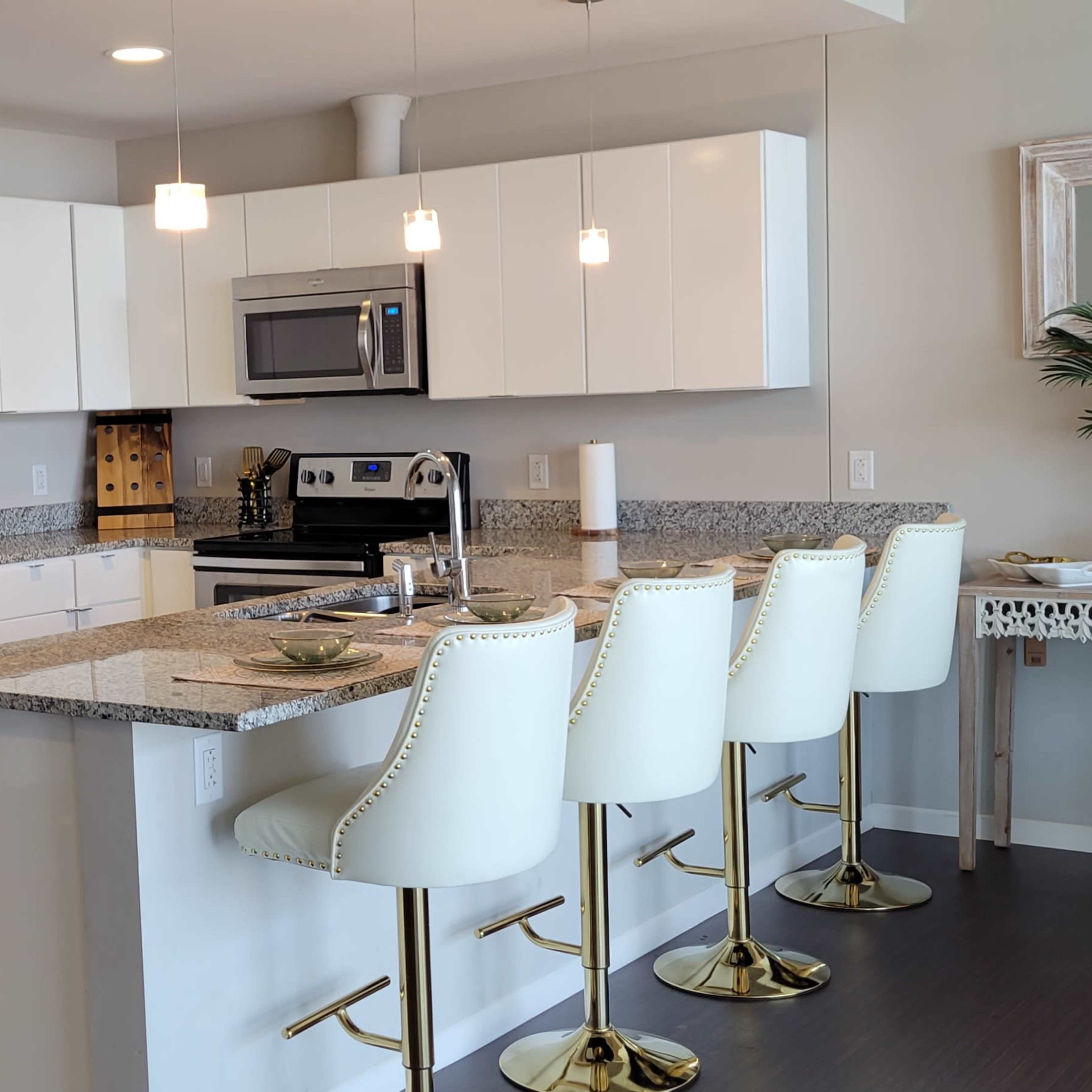 A modern kitchen equipped with white cabinets, stainless steel appliances, a granite countertop, and four bar stools.