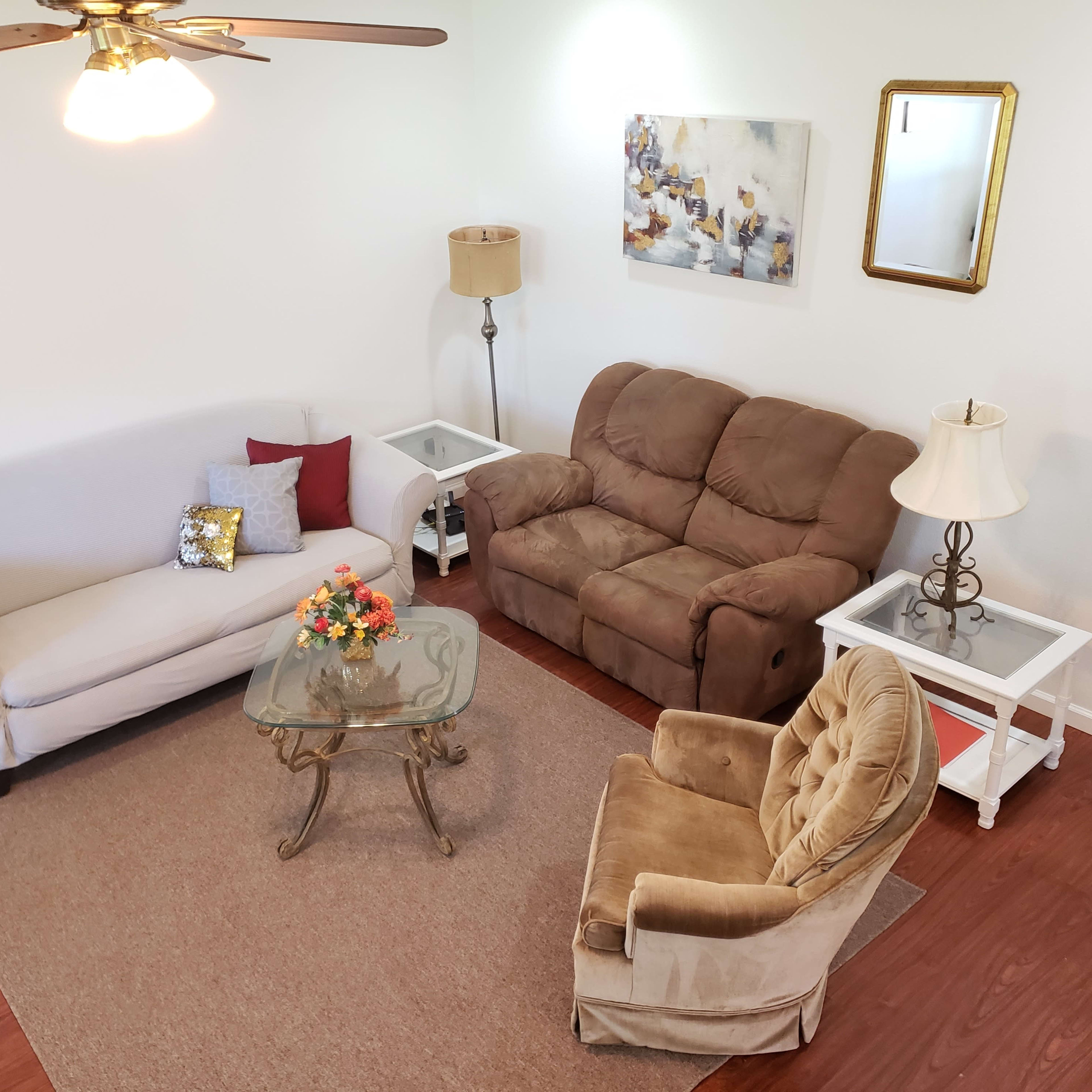 A living room with a light-colored sofa, a brown loveseat, a glass coffee table, and a beige rug.