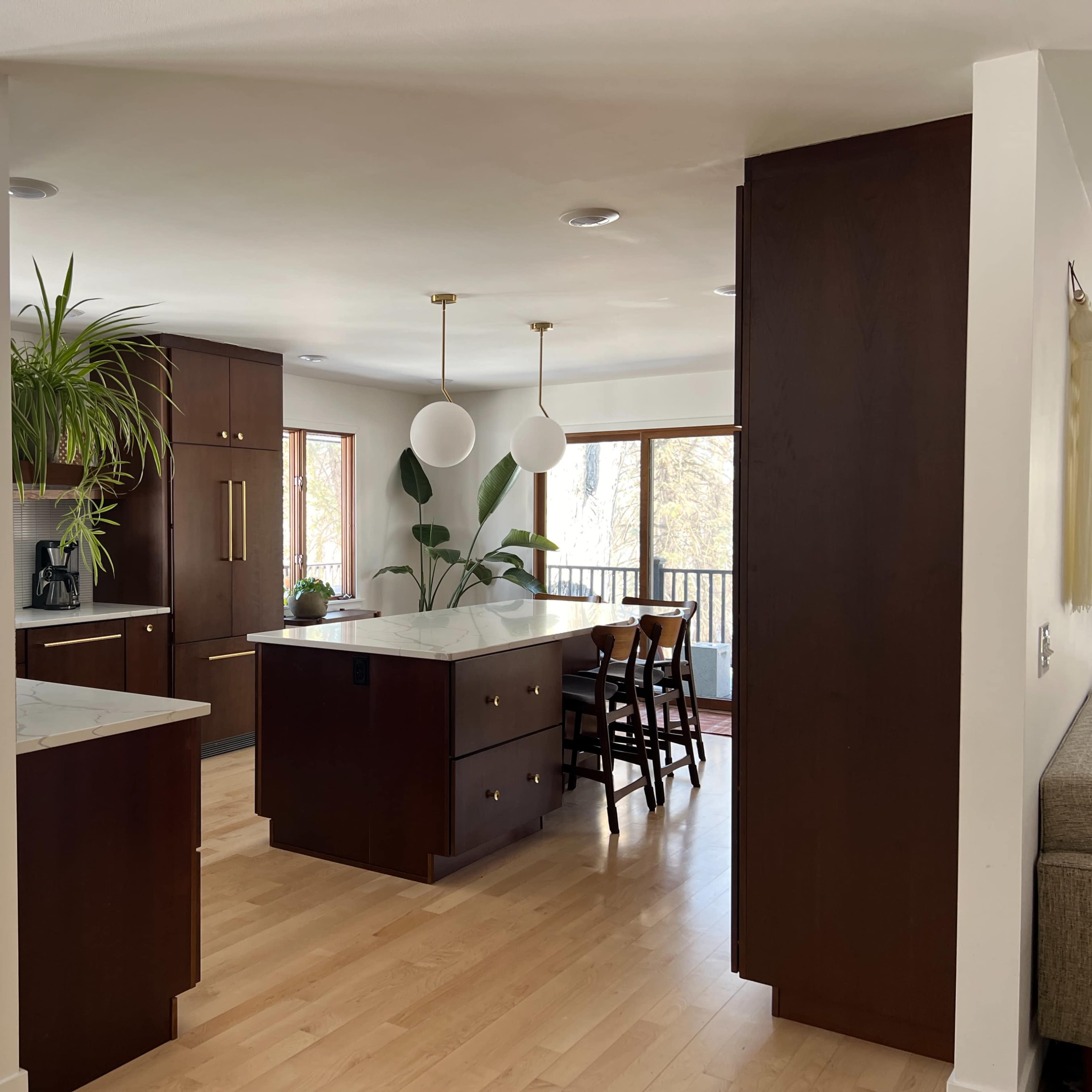 A modern kitchen with dark wood cabinets, a central island, and a dining area featuring large windows and a view.